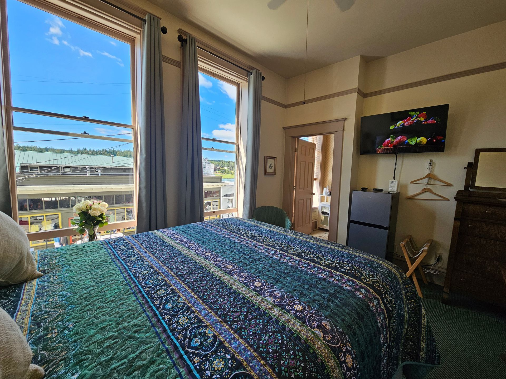 A bedroom with a bed , dresser , television and large window.