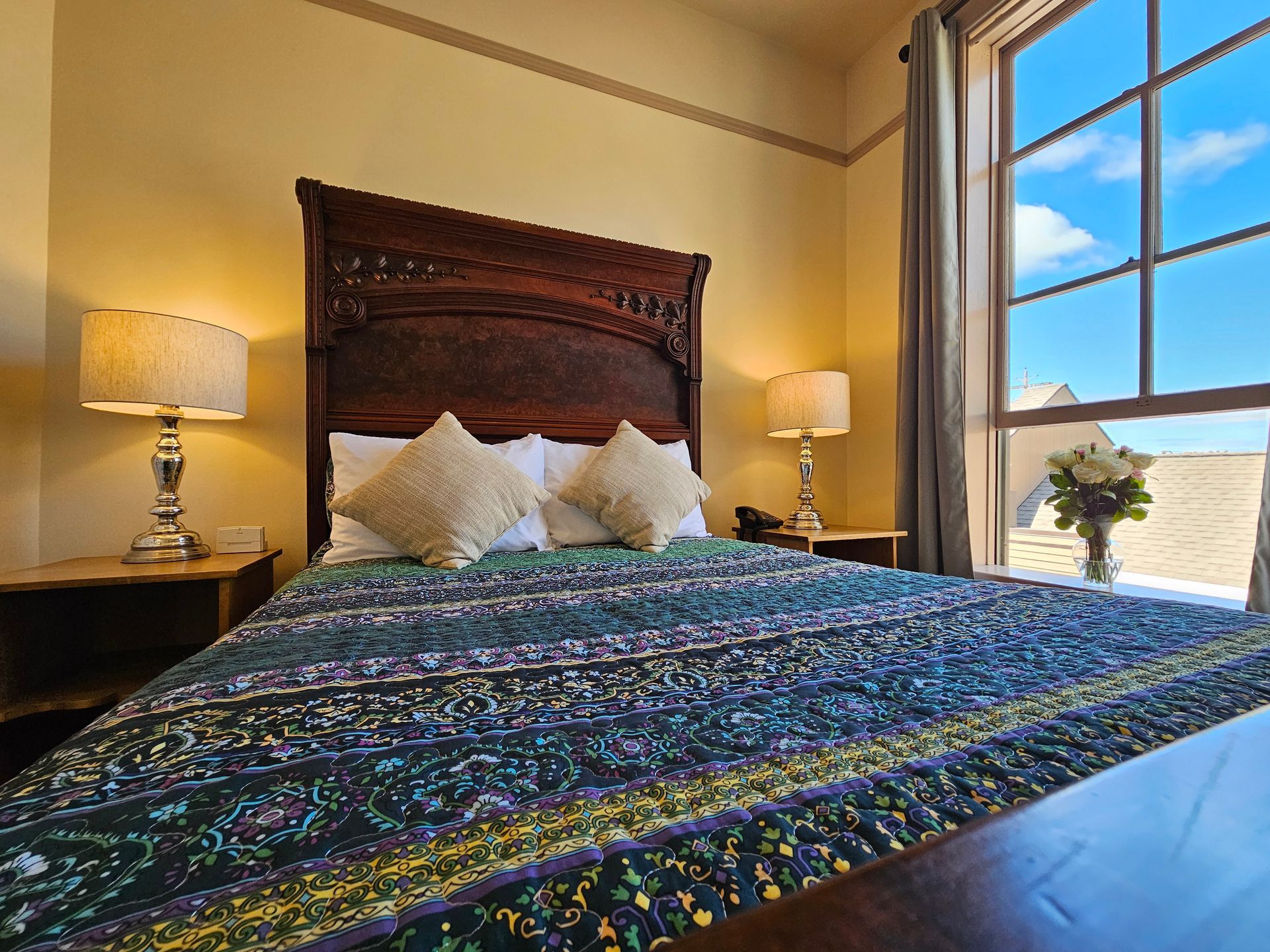 A hotel room with a bed , two lamps , and a large window.