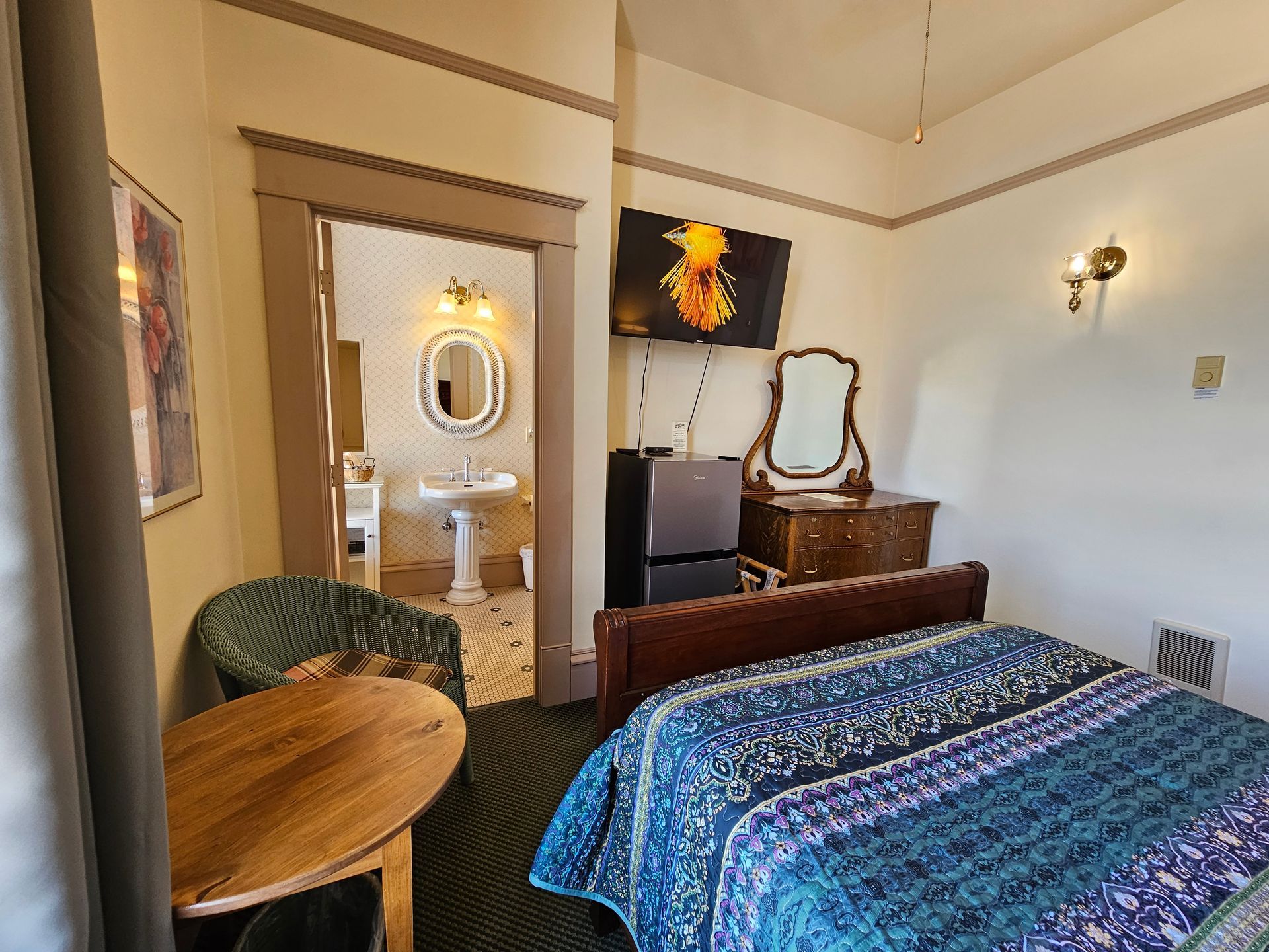 A hotel room with a bed , dresser , chair , table and television.