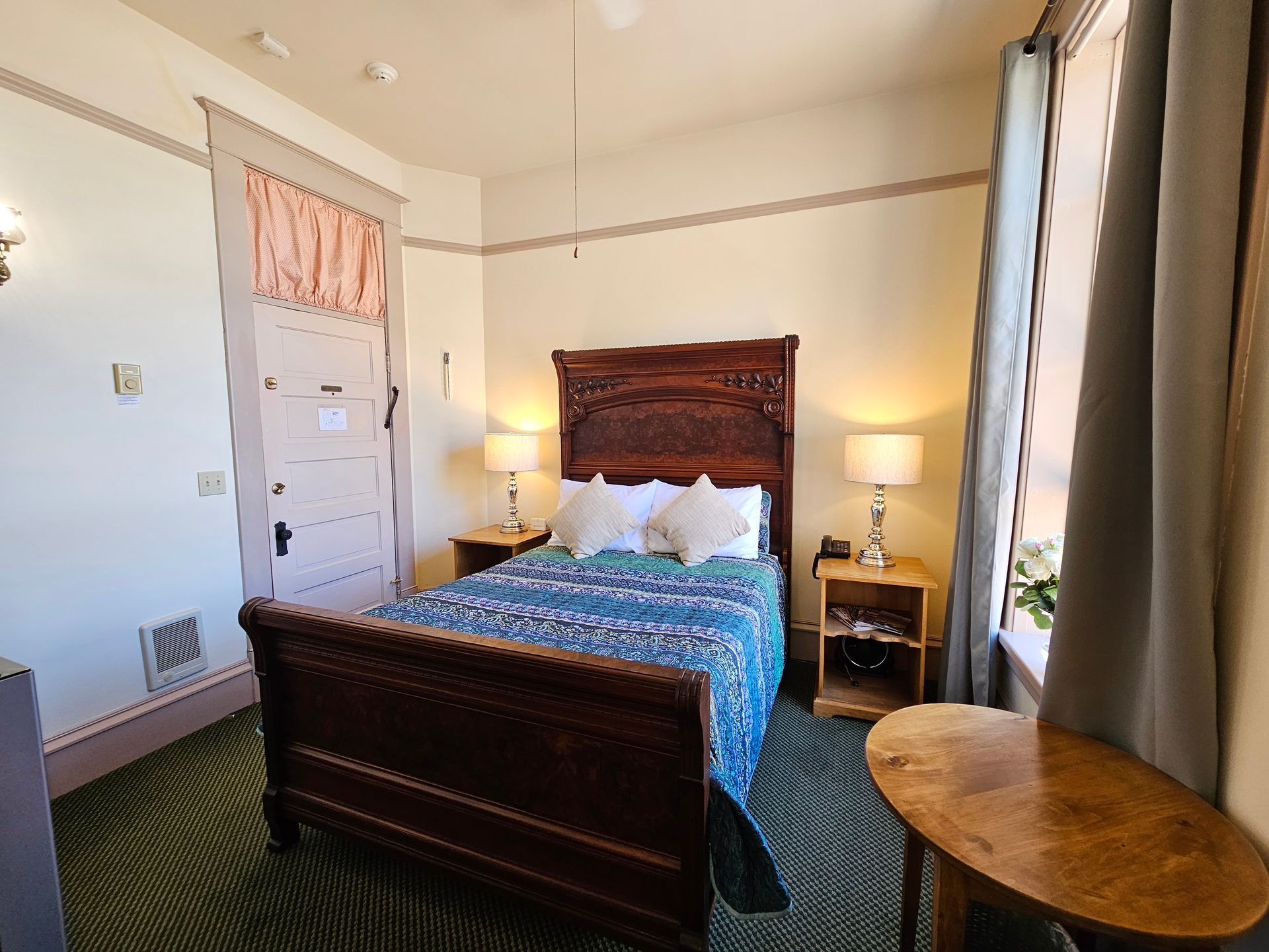 A bedroom with a bed , two nightstands , a table and a window.