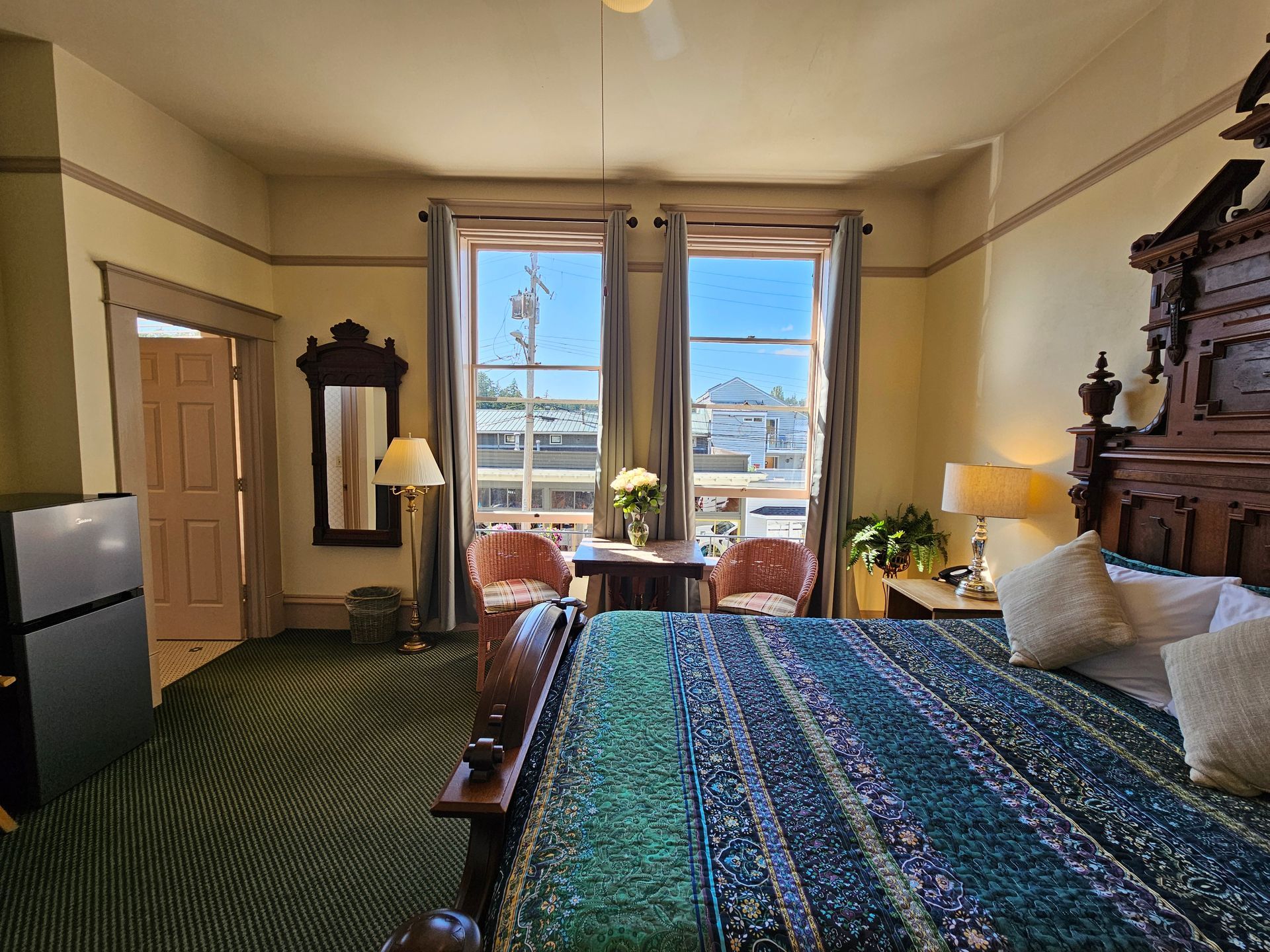 A bedroom with a king size bed , two chairs , a table and a mirror.