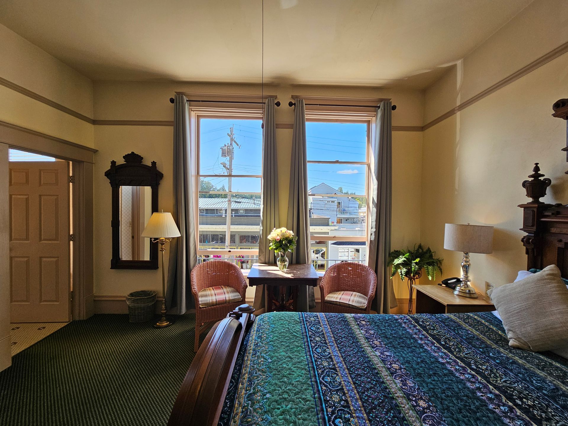 A hotel room with a bed , chairs , lamps and a large window.