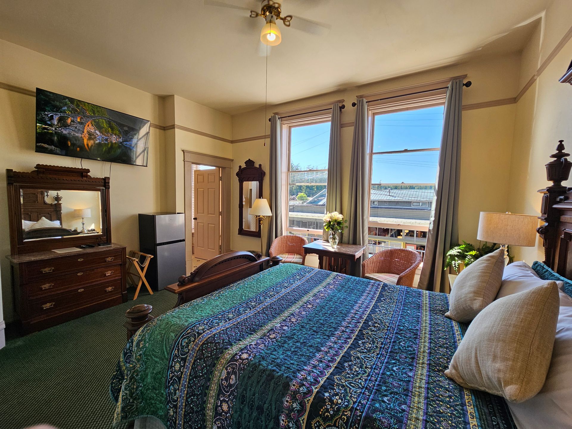 A hotel room with a king size bed , dresser , chairs , and a television.