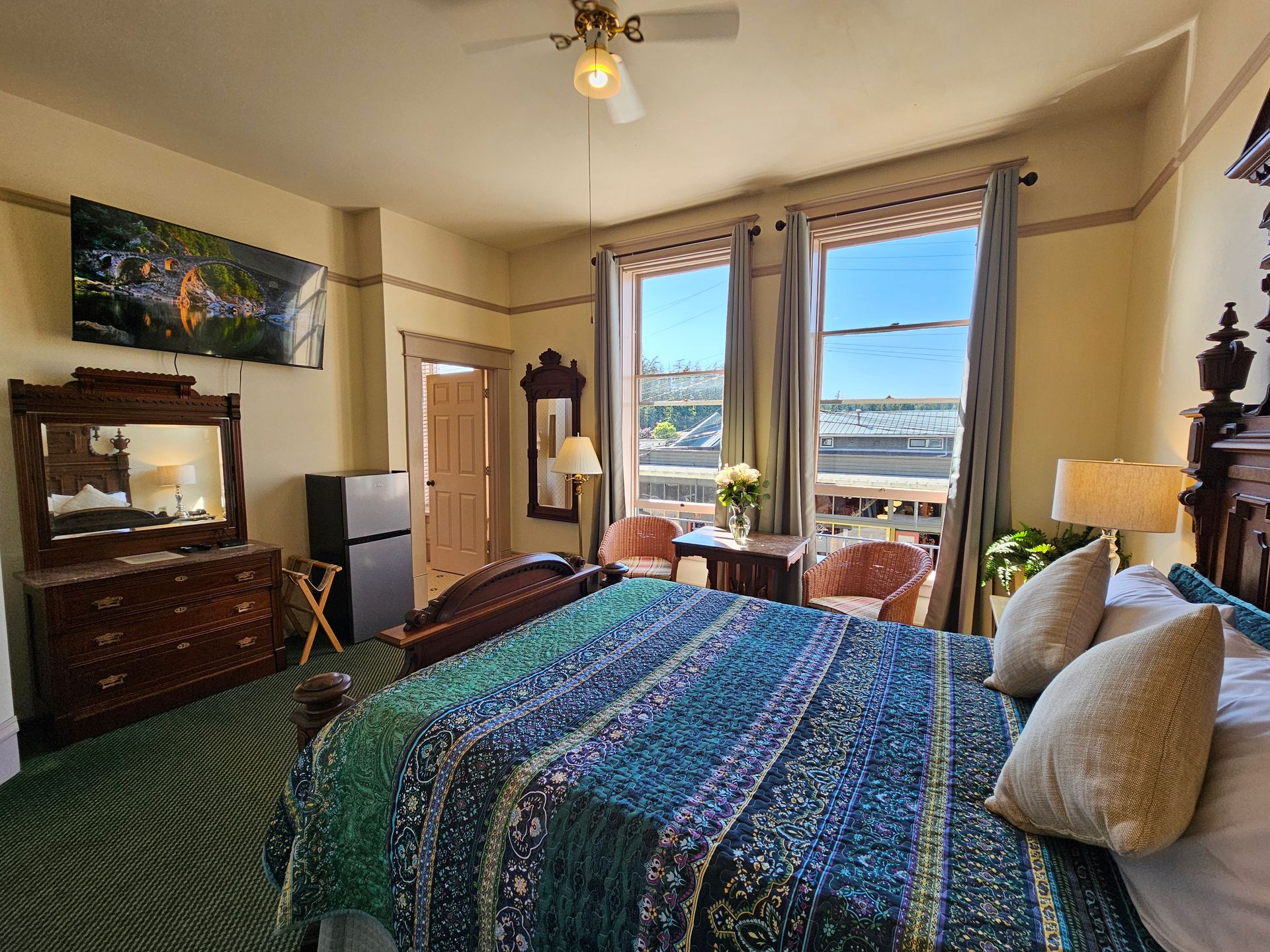 A hotel room with a king size bed , dresser , mirror and television.