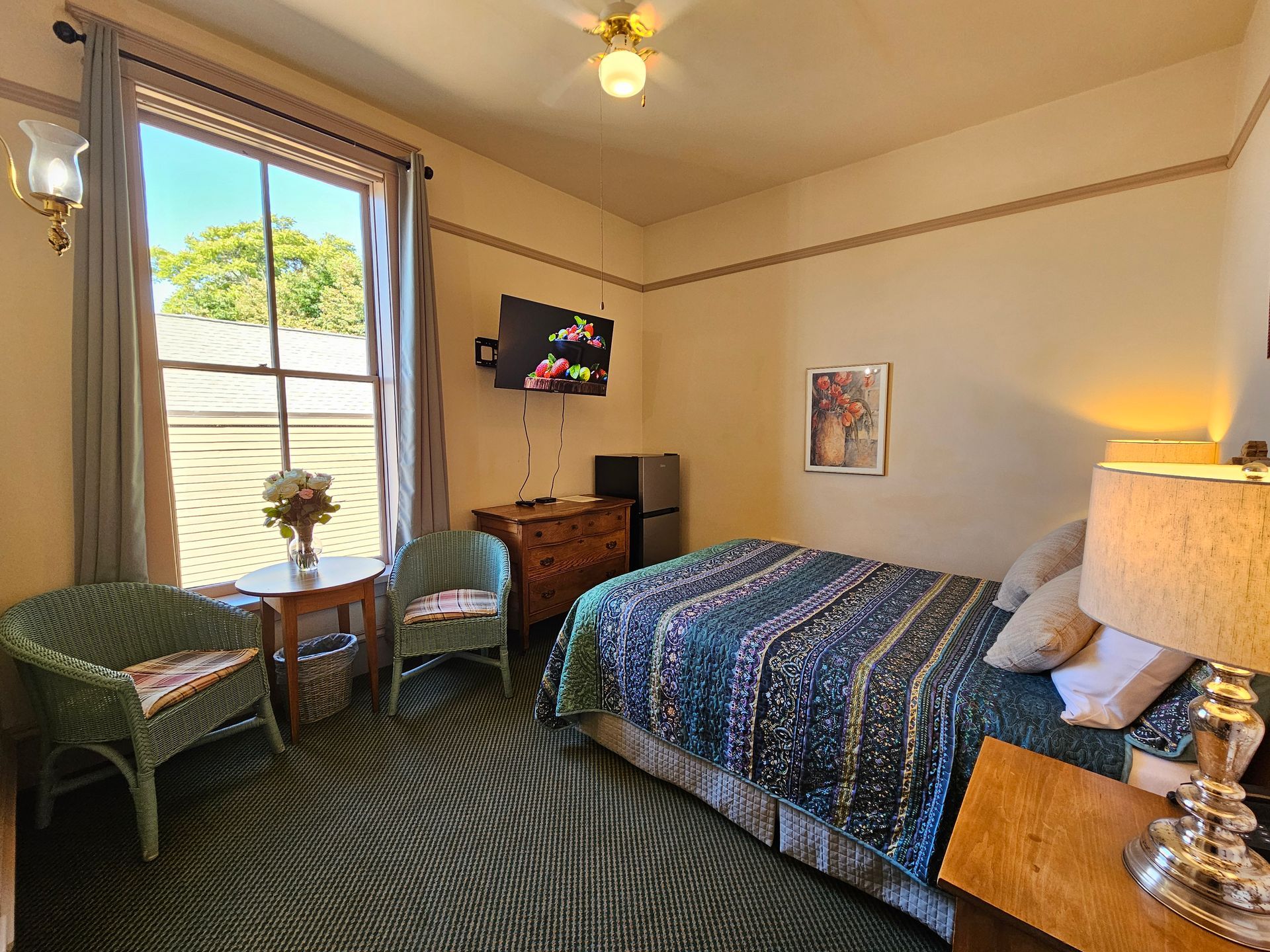 A hotel room with a bed , chairs , a table and a television.