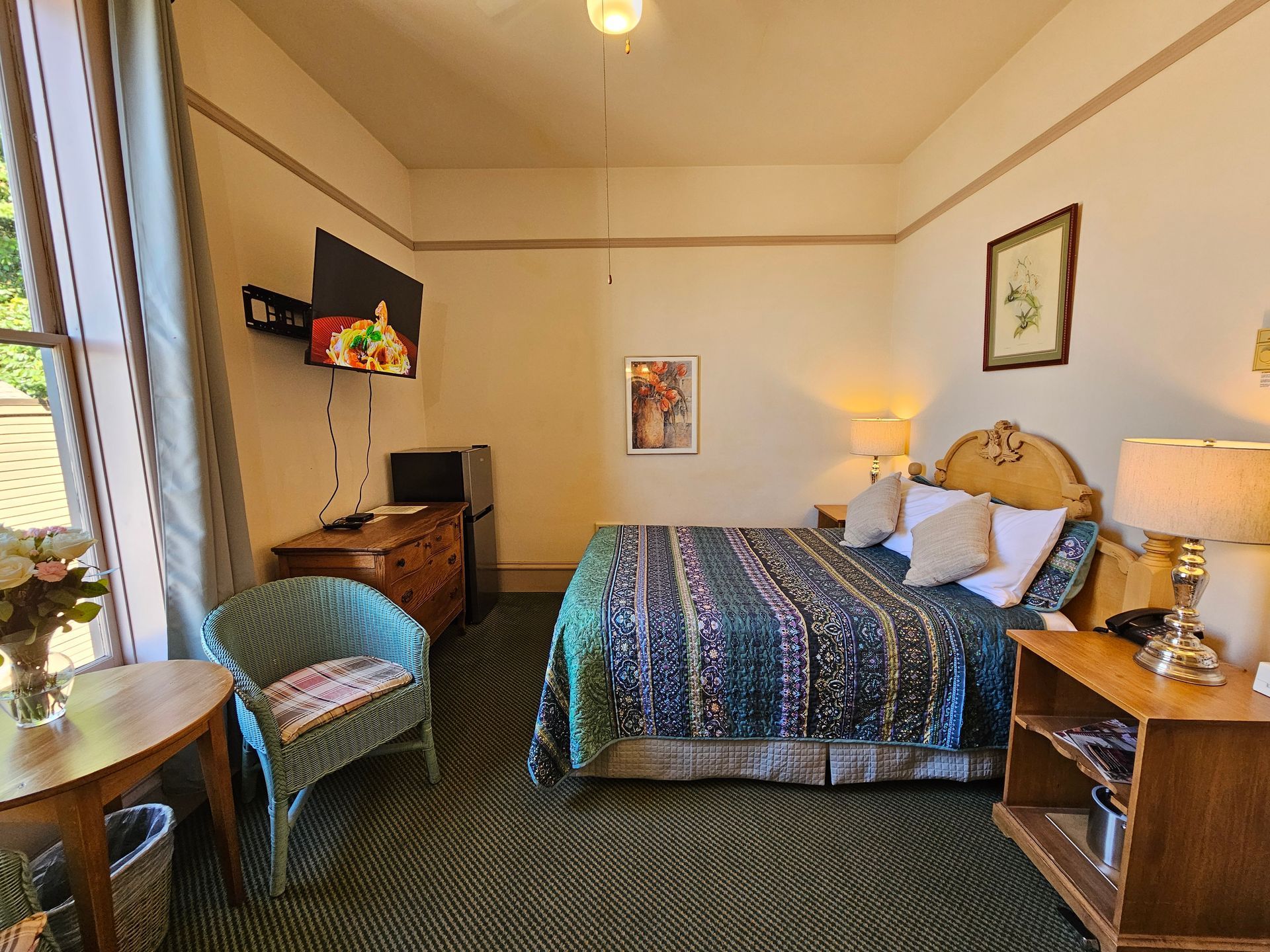 A hotel room with a bed , chair , nightstand , table and television.