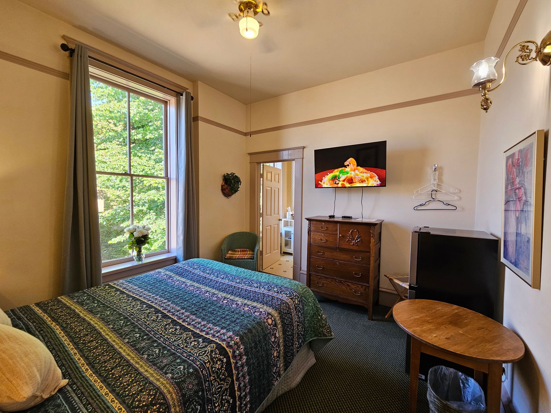 A bedroom with a bed , dresser , table and television.