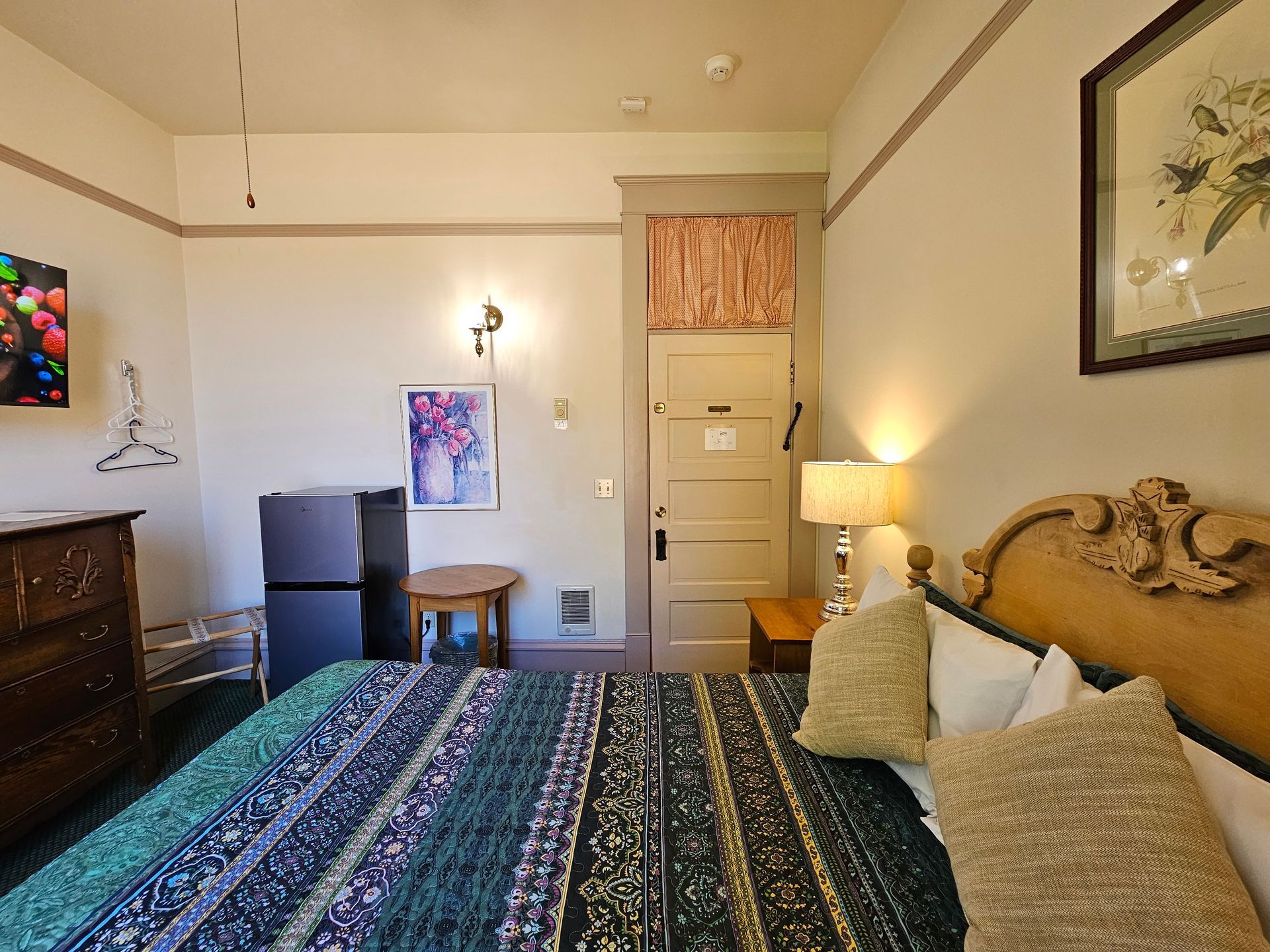 A hotel room with a bed , dresser , refrigerator and television.