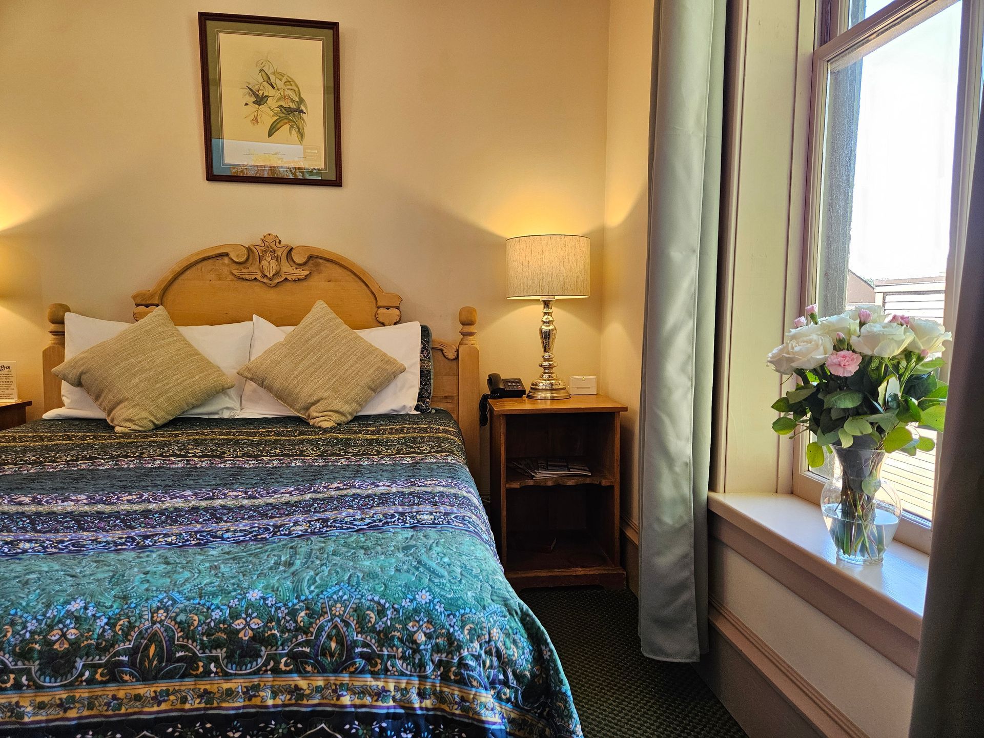 A hotel room with a bed , nightstand , lamp and window.