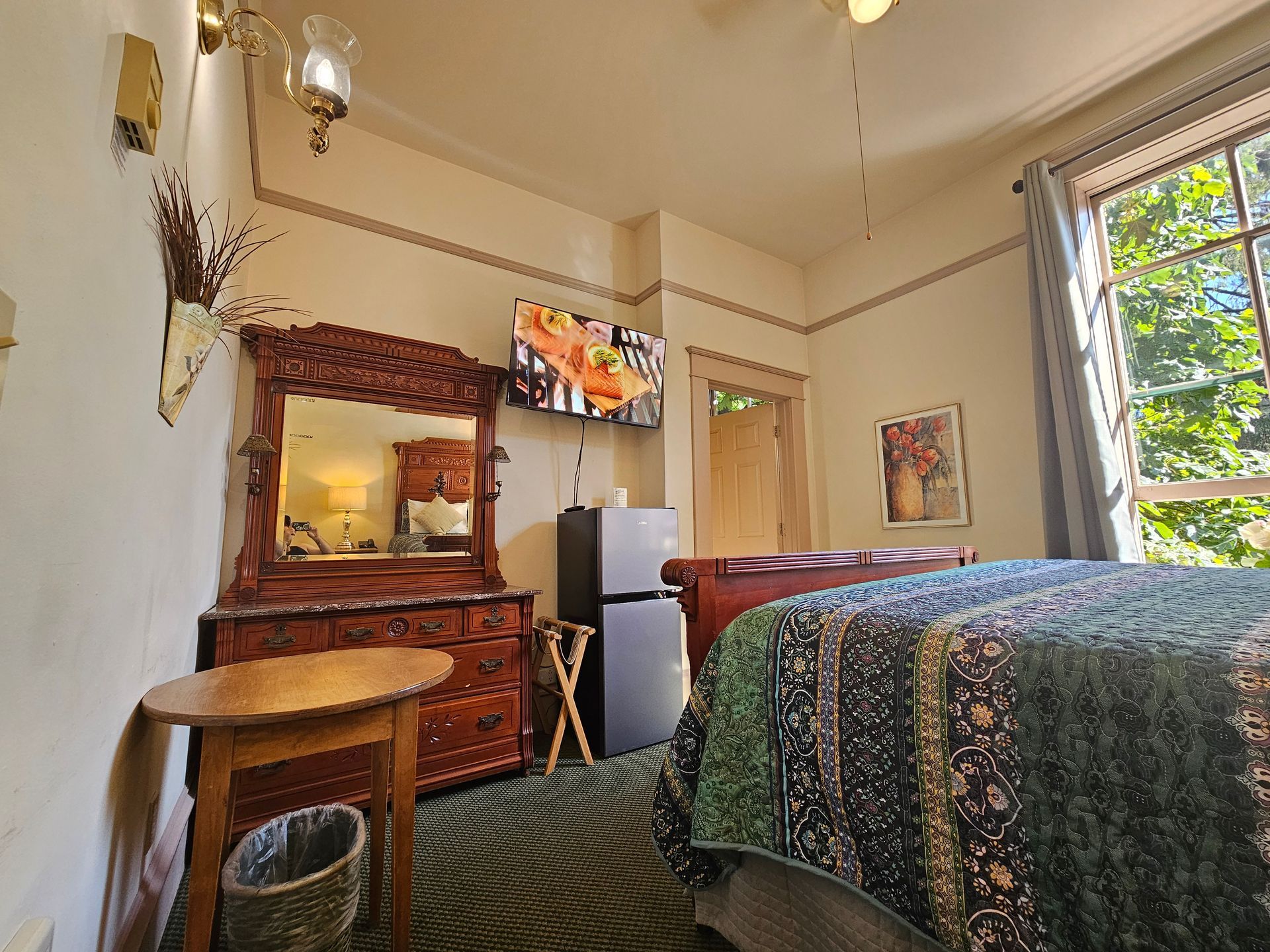 A hotel room with a bed , dresser , table and television.