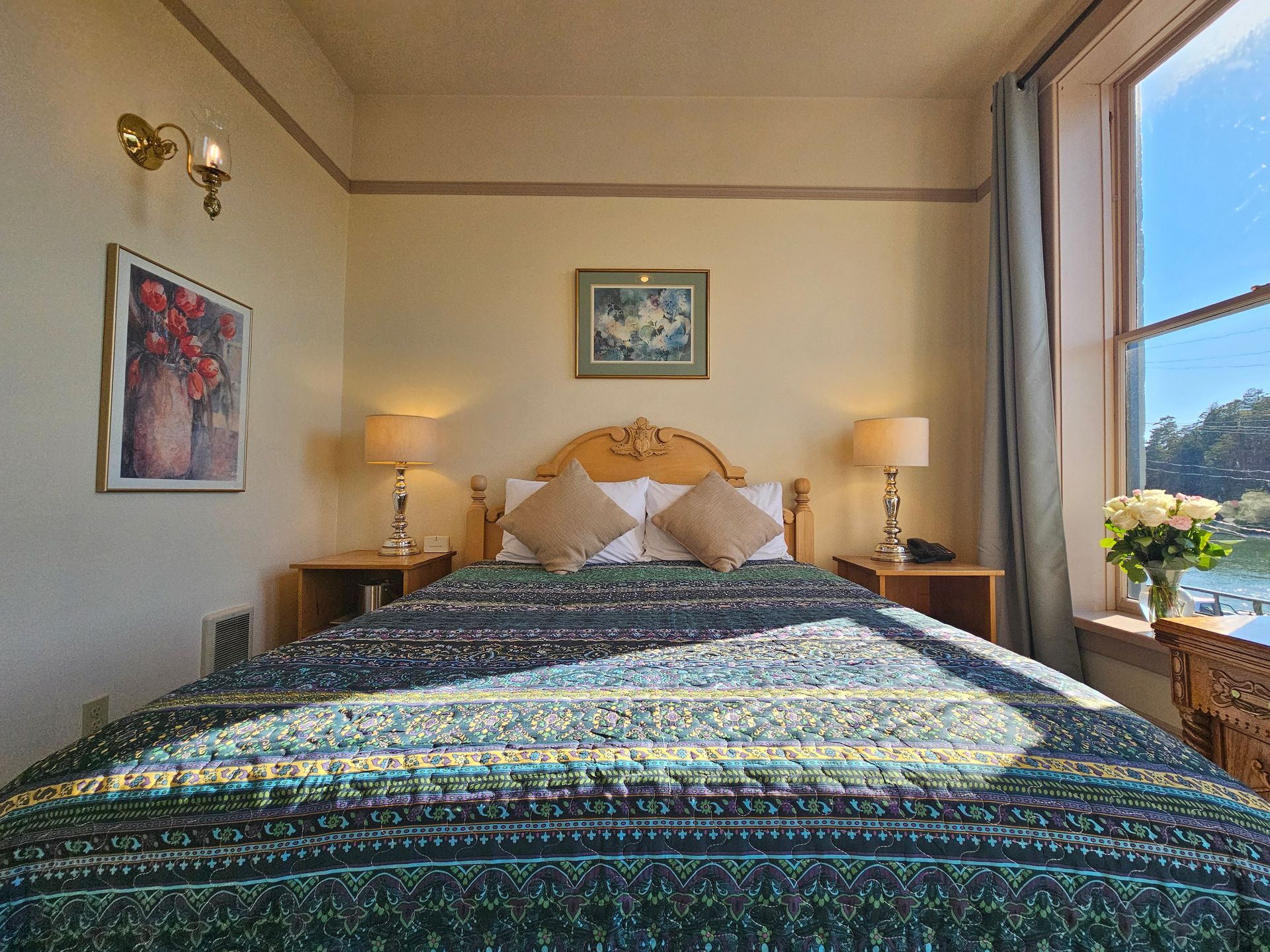 A hotel room with a bed , lamps , a picture on the wall and a window.