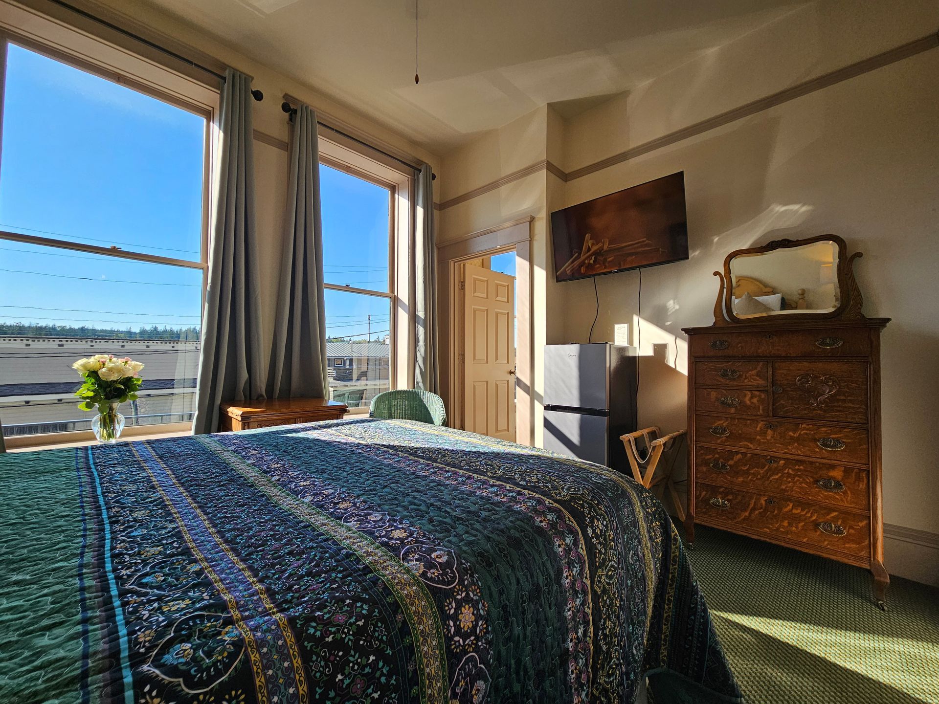 A bedroom with a bed , dresser , mirror and window.