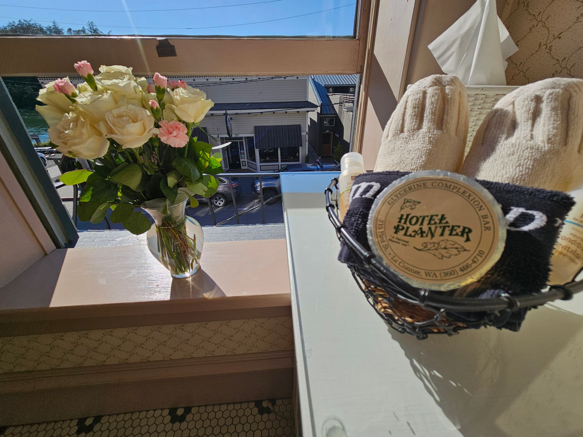 A vase of flowers sits next to a basket of towels and slippers.