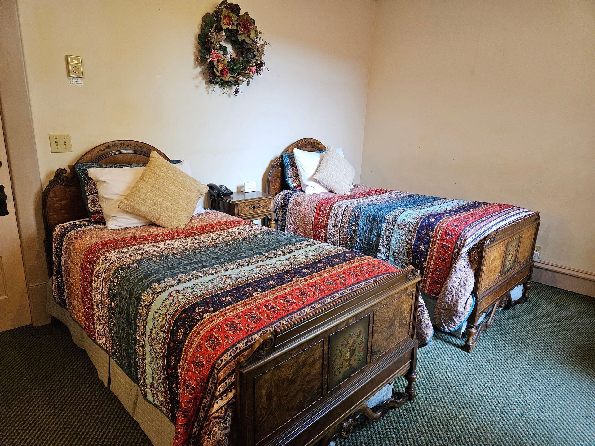 A bedroom with two beds and a wreath on the wall.