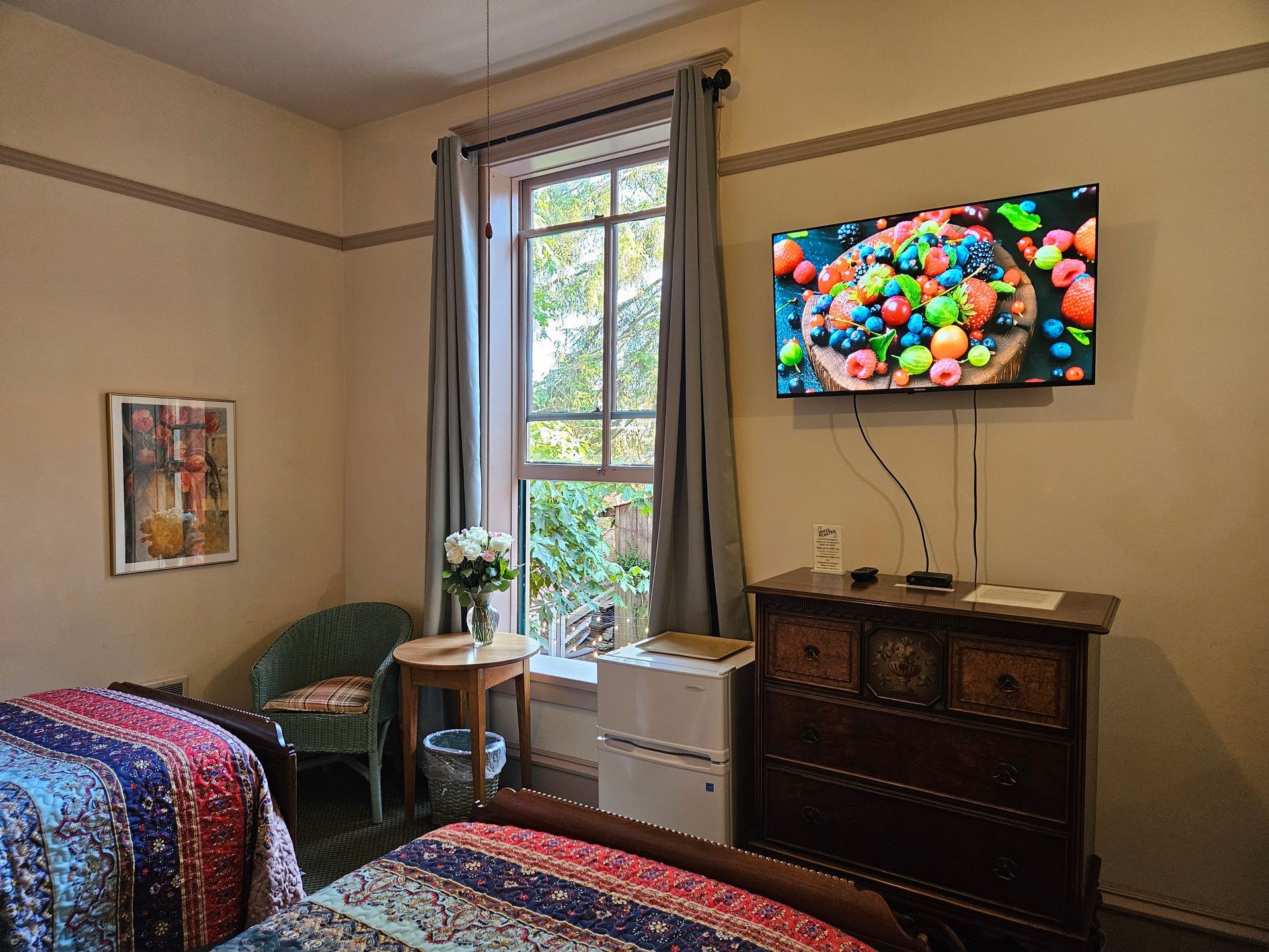 A bedroom with two beds , a dresser , a television and a window.