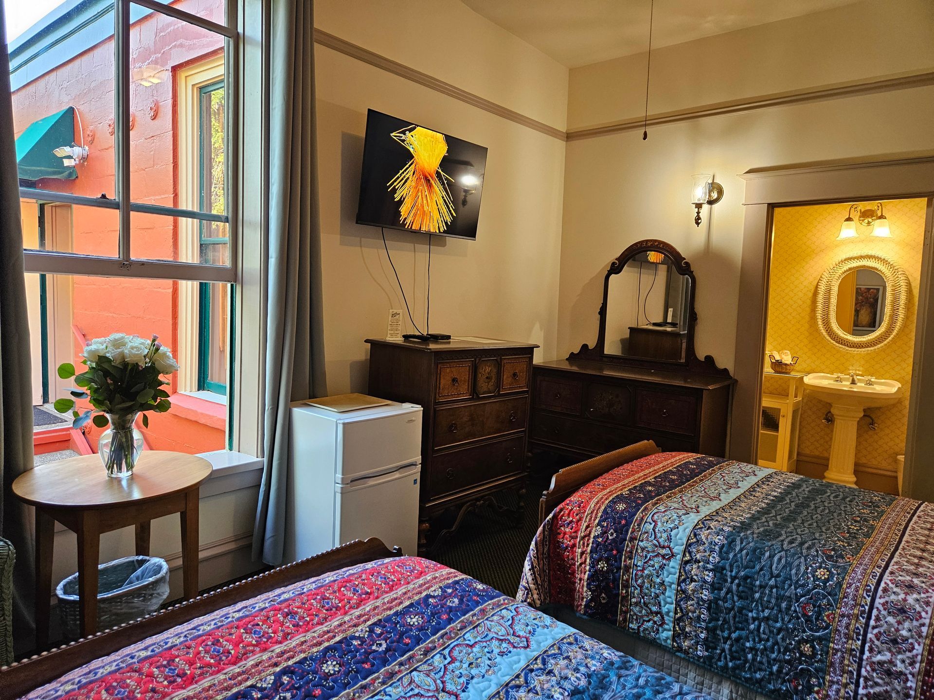 A hotel room with two beds , a dresser , a television and a sink.