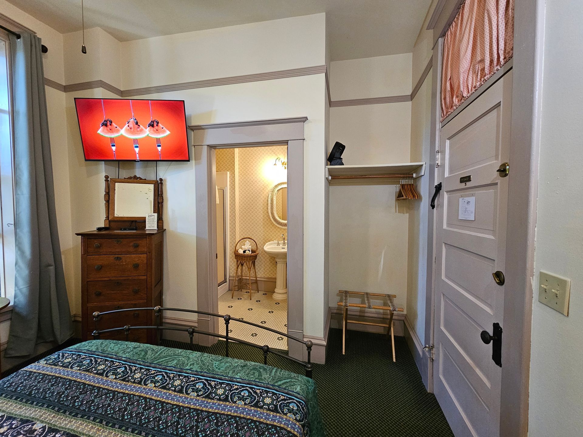 A bedroom with a bed , dresser , television and a bathroom.