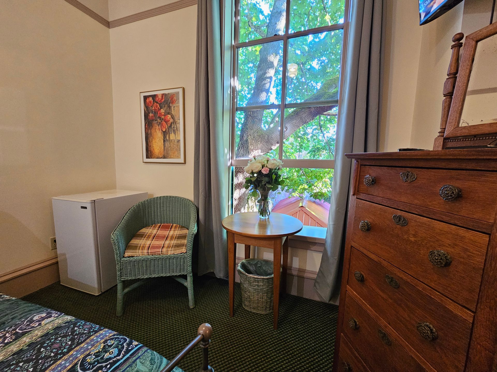 A bedroom with a bed , dresser , chair , table and window.