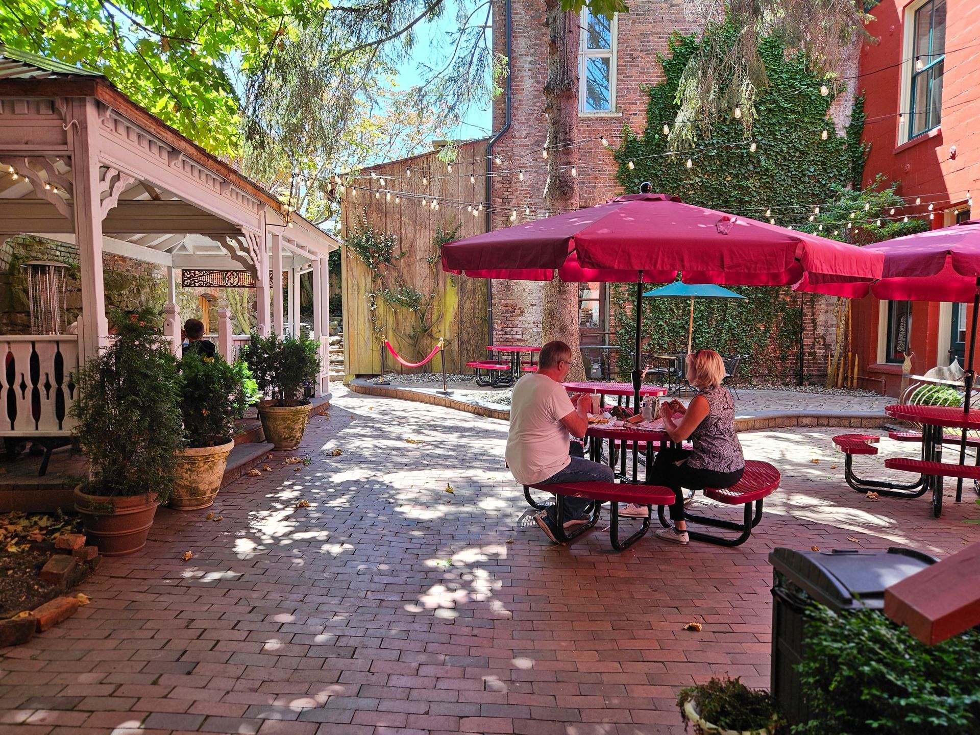 A man and a woman are sitting at a picnic table under red umbrellas.