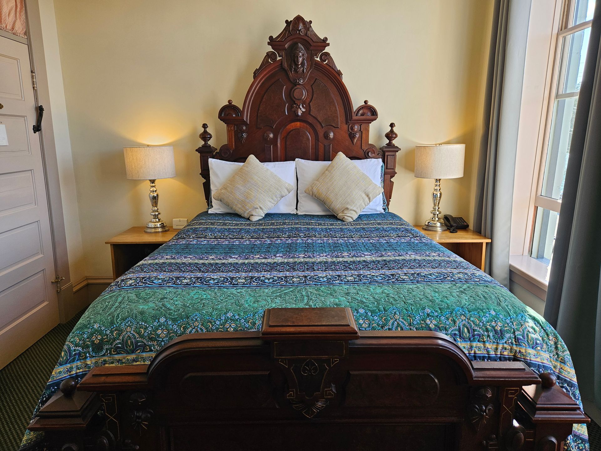 Large antique carved bed with a green and blue quilt on top.