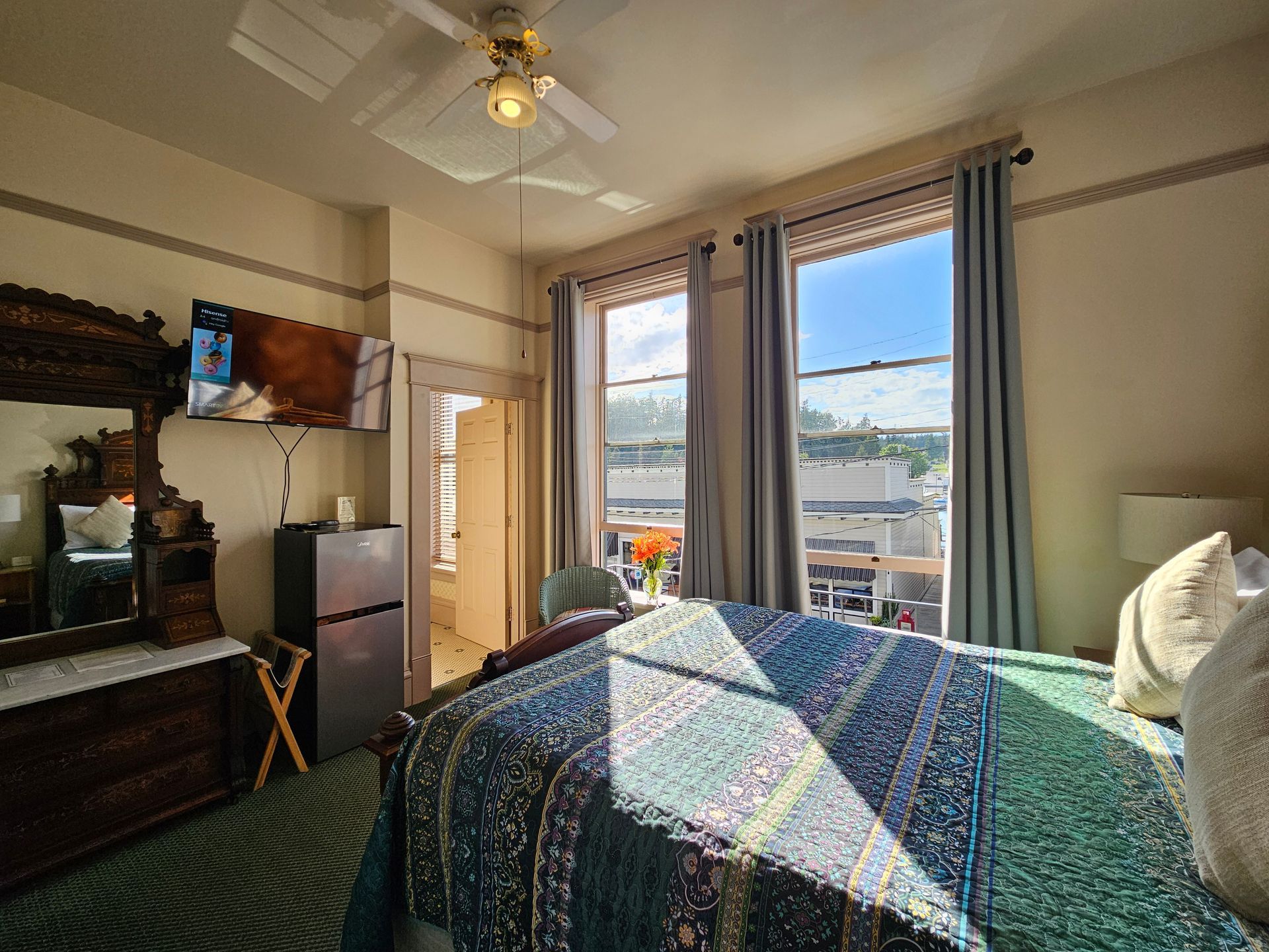 Bedroom with large bed, two windows, dresser, fridge, and TV. 