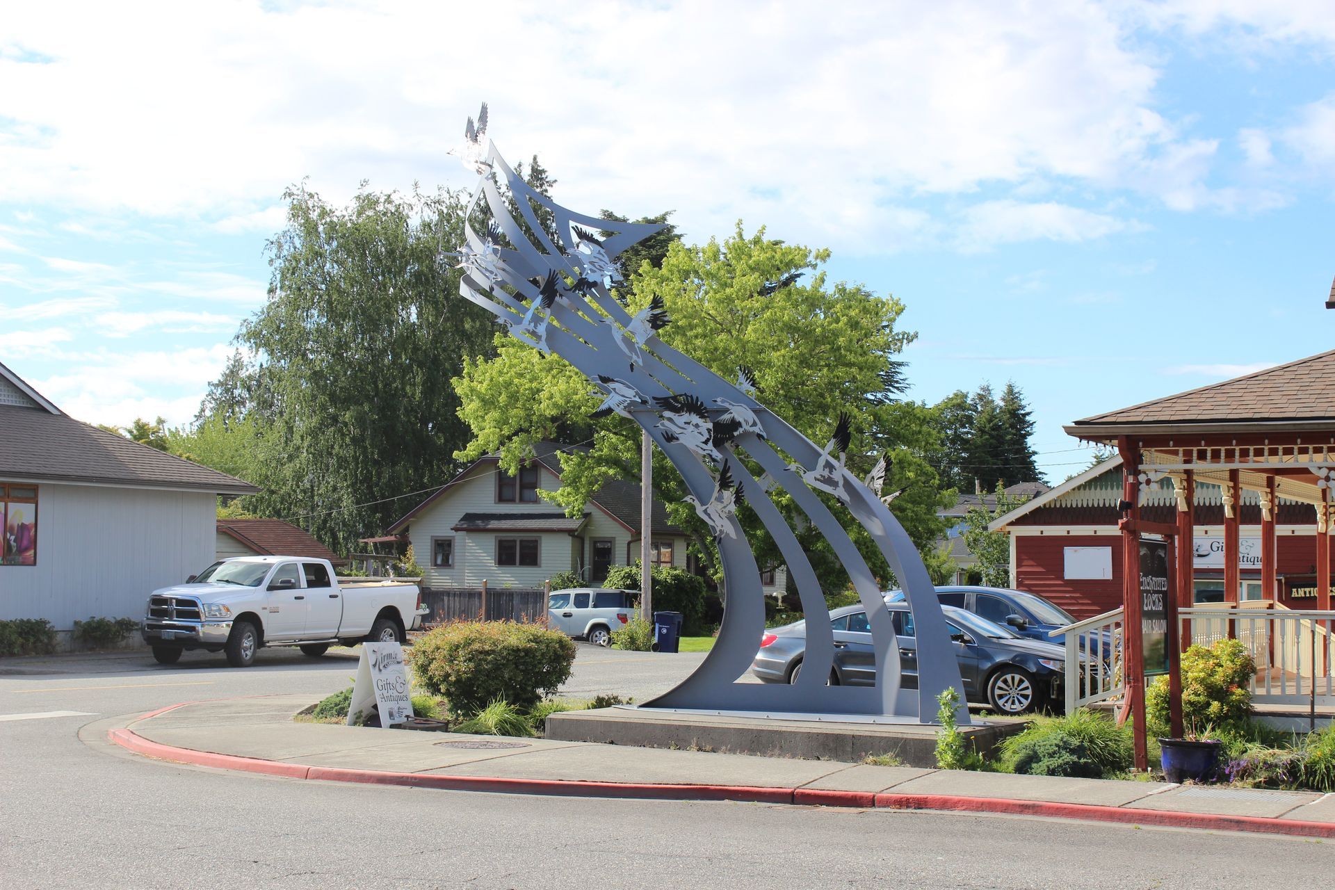 A statue of a wave is in the middle of a street in a small town.