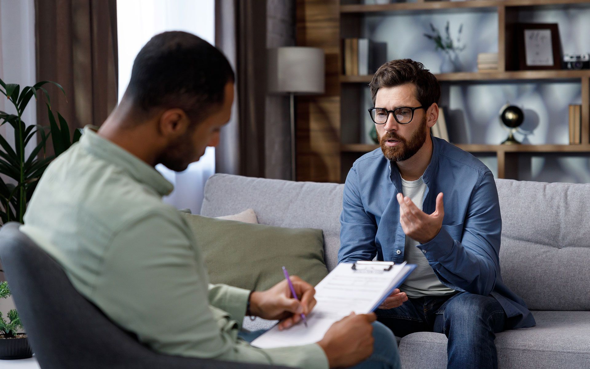 A man is sitting on a couch talking to another man.