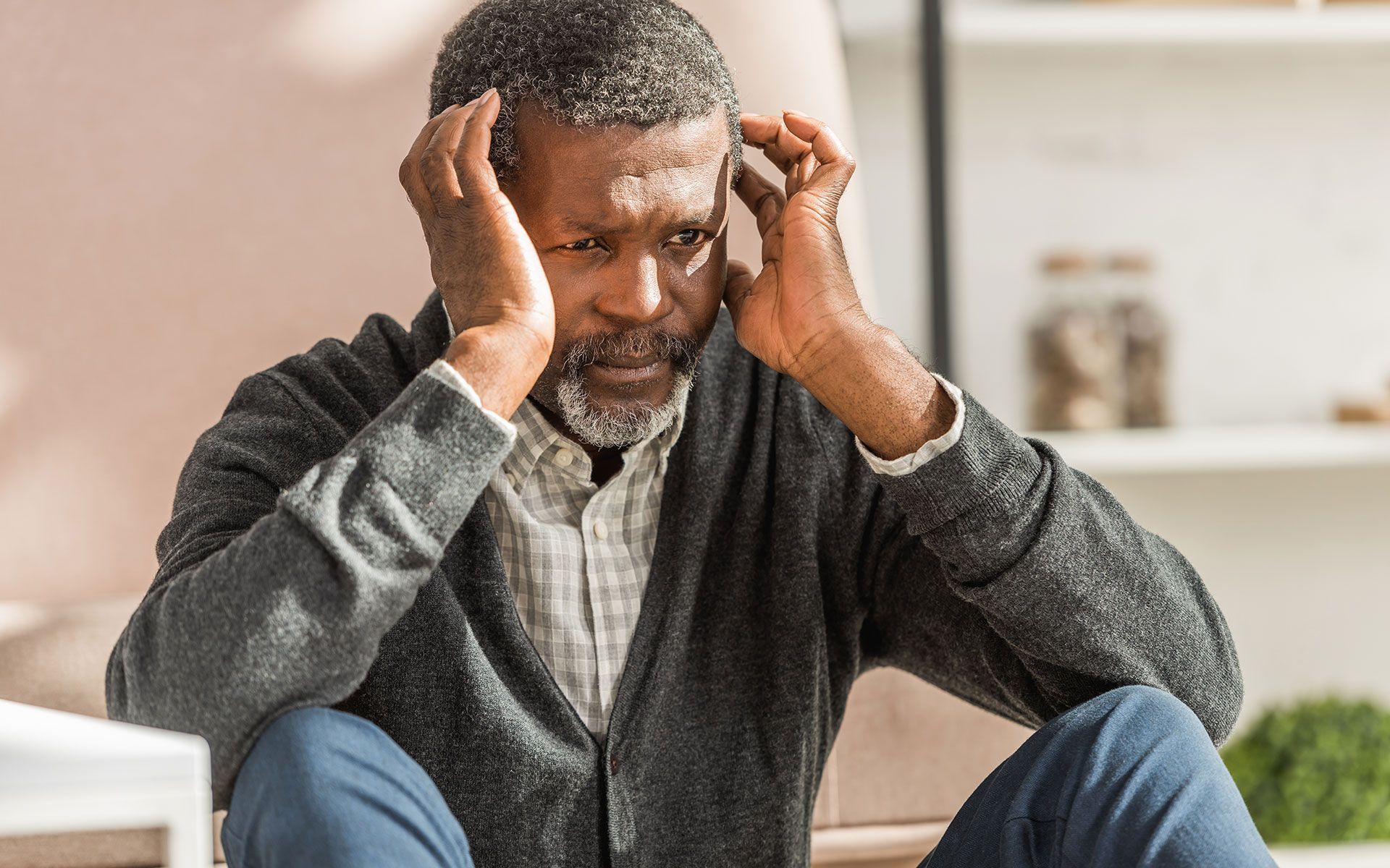 A man is sitting on the floor with his hands on his head.