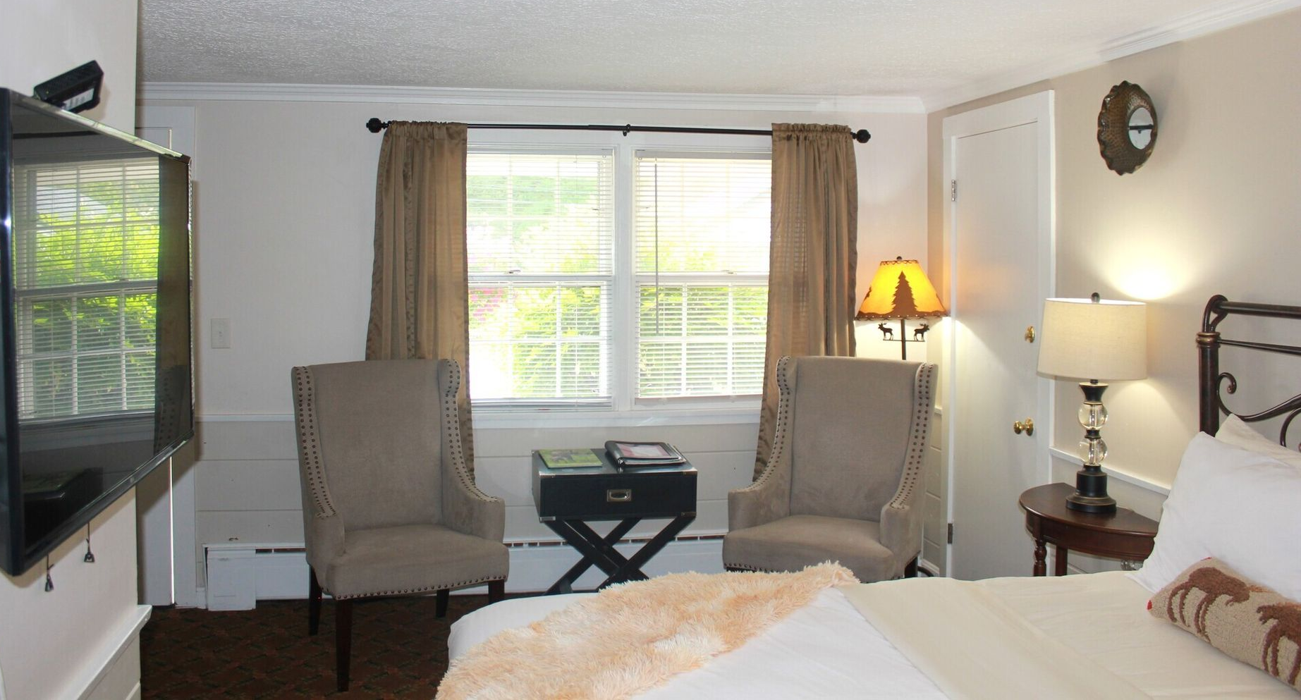 Cozy hotel room with two armchairs, a small table, a window with curtains, and a TV.