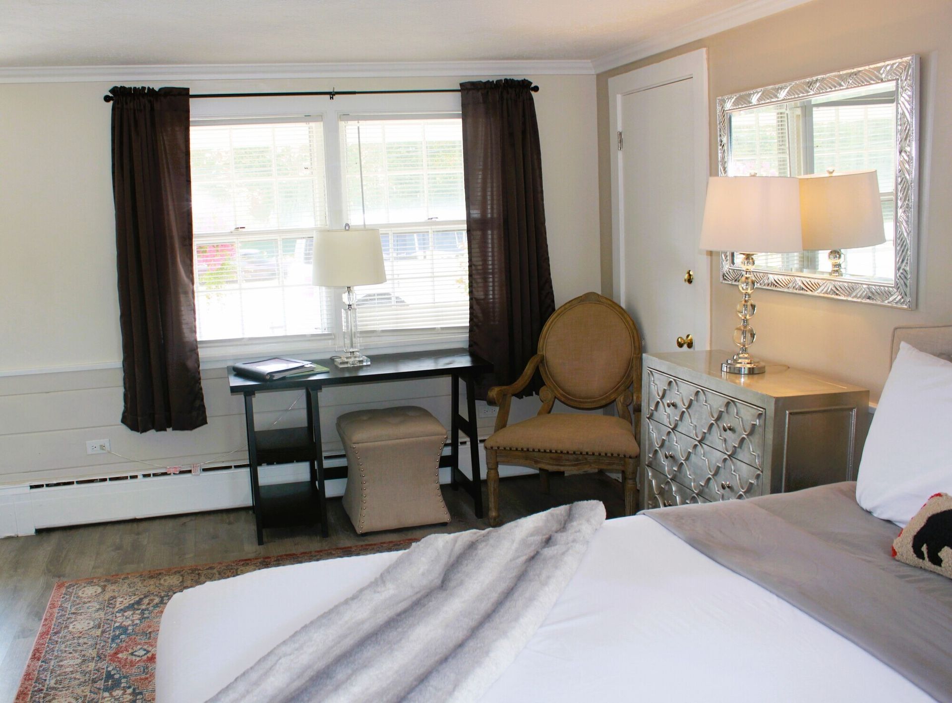 Bedroom with bed, desk, chair, window, mirror, and neutral-toned décor.