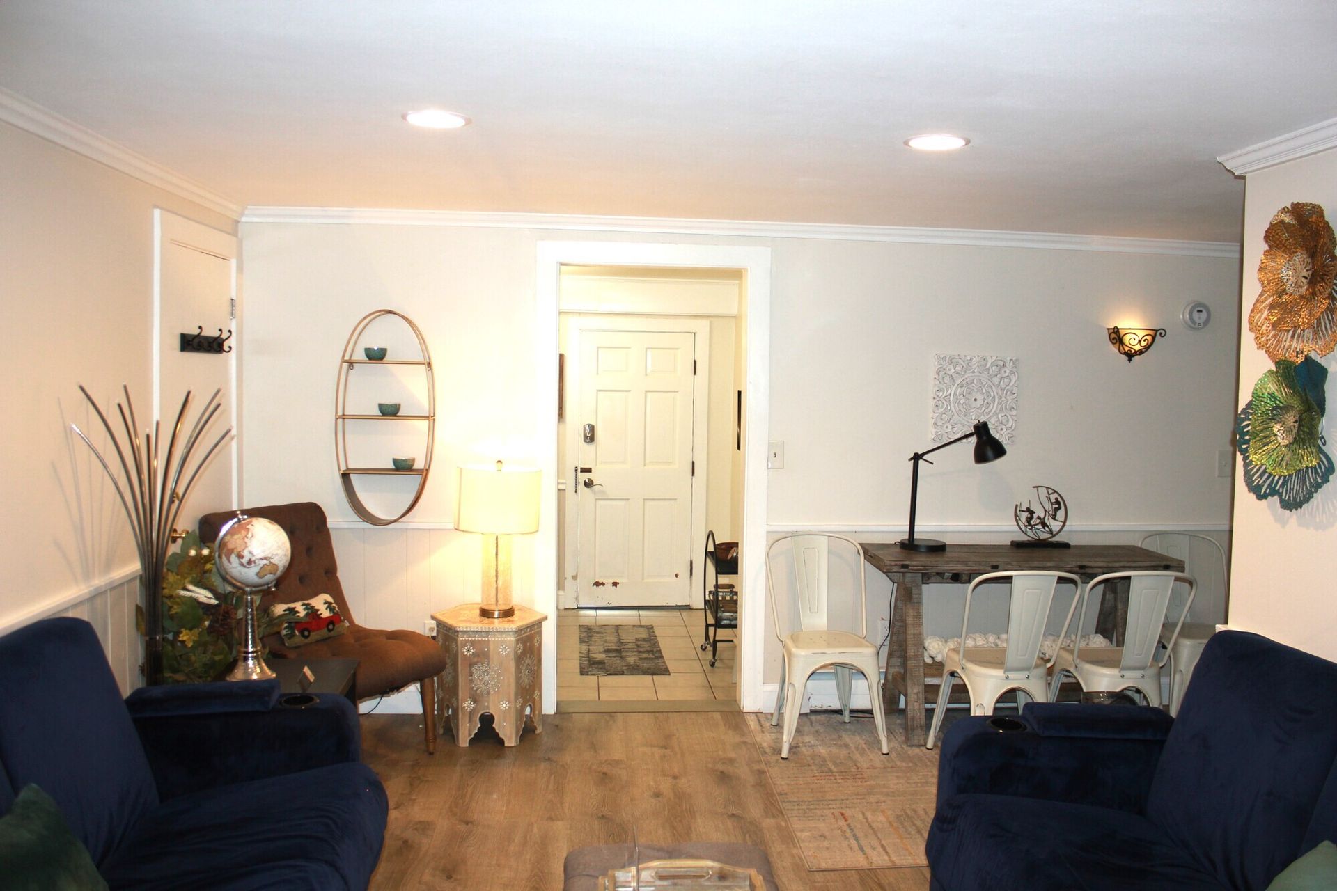 Living room with white walls, wood floors, and blue sofas. A desk and chair sit near the doorway.