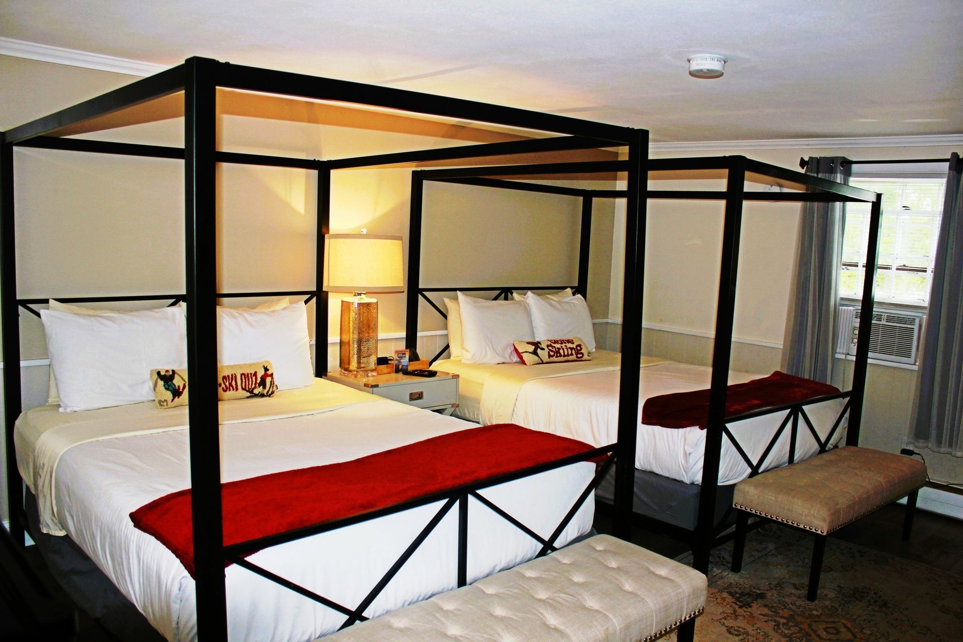 Two beds with black canopy frames, red accents, and a beige bench in a hotel room.