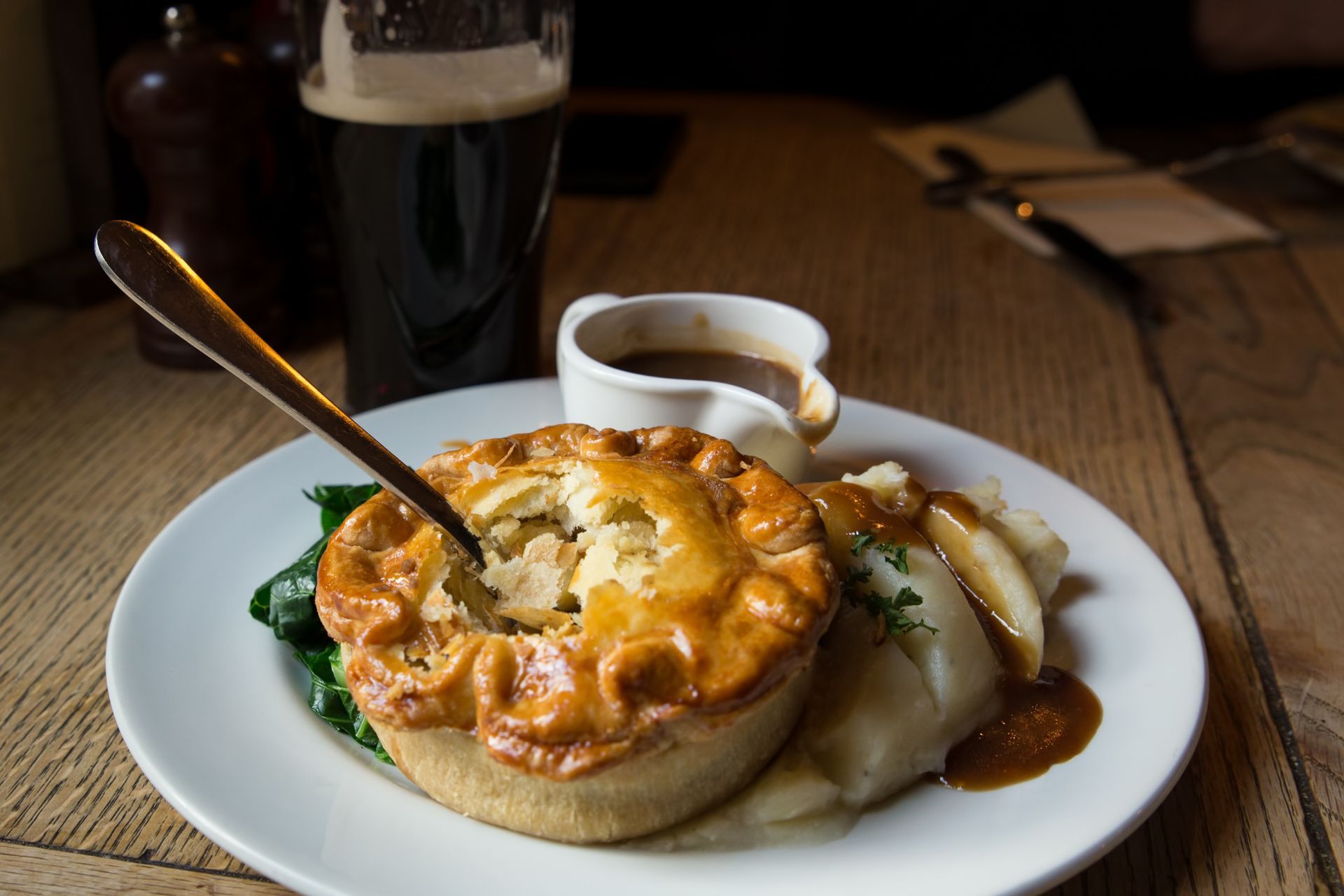 Meat pie with mashed potatoes, gravy, and dark beer on a wooden table.