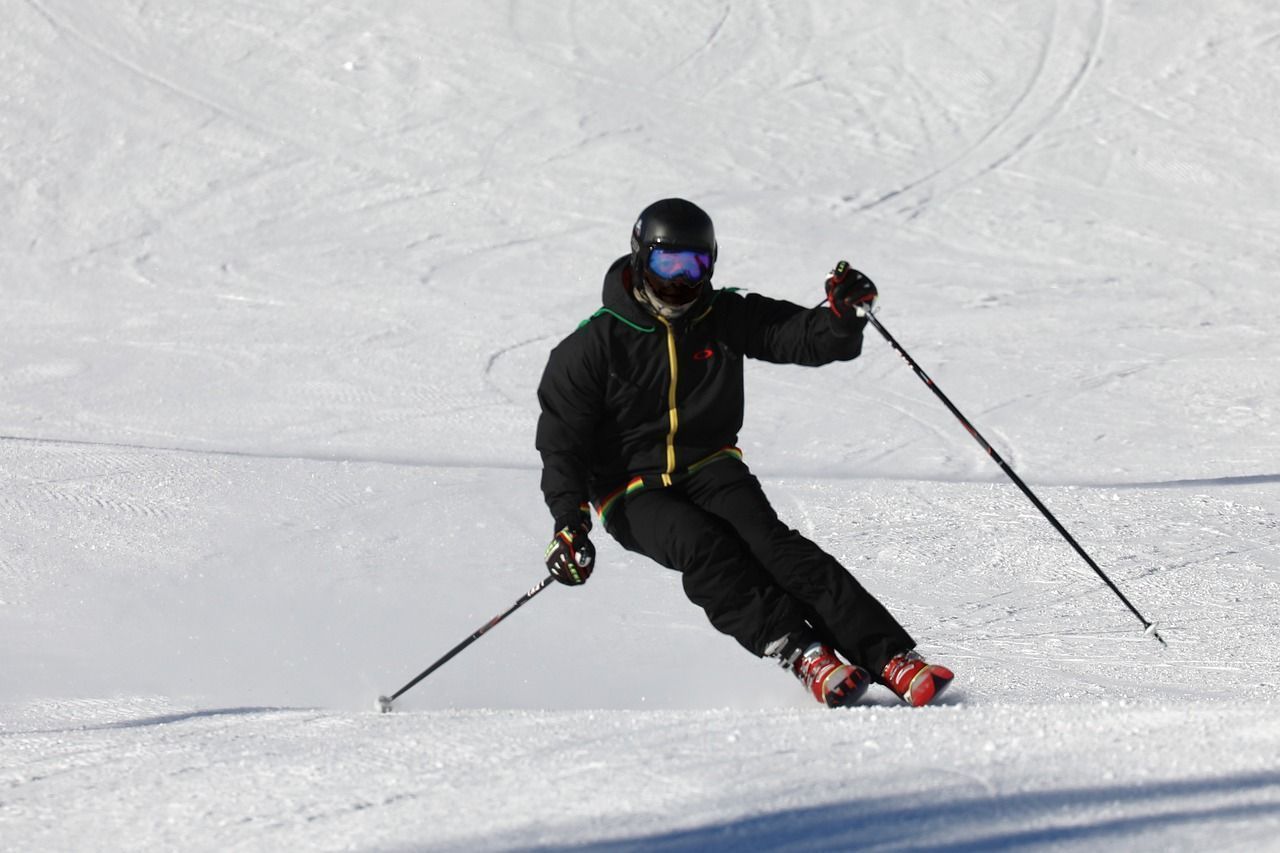 Skier in black gear carves down a snow-covered slope, poles extended, helmet and goggles on.