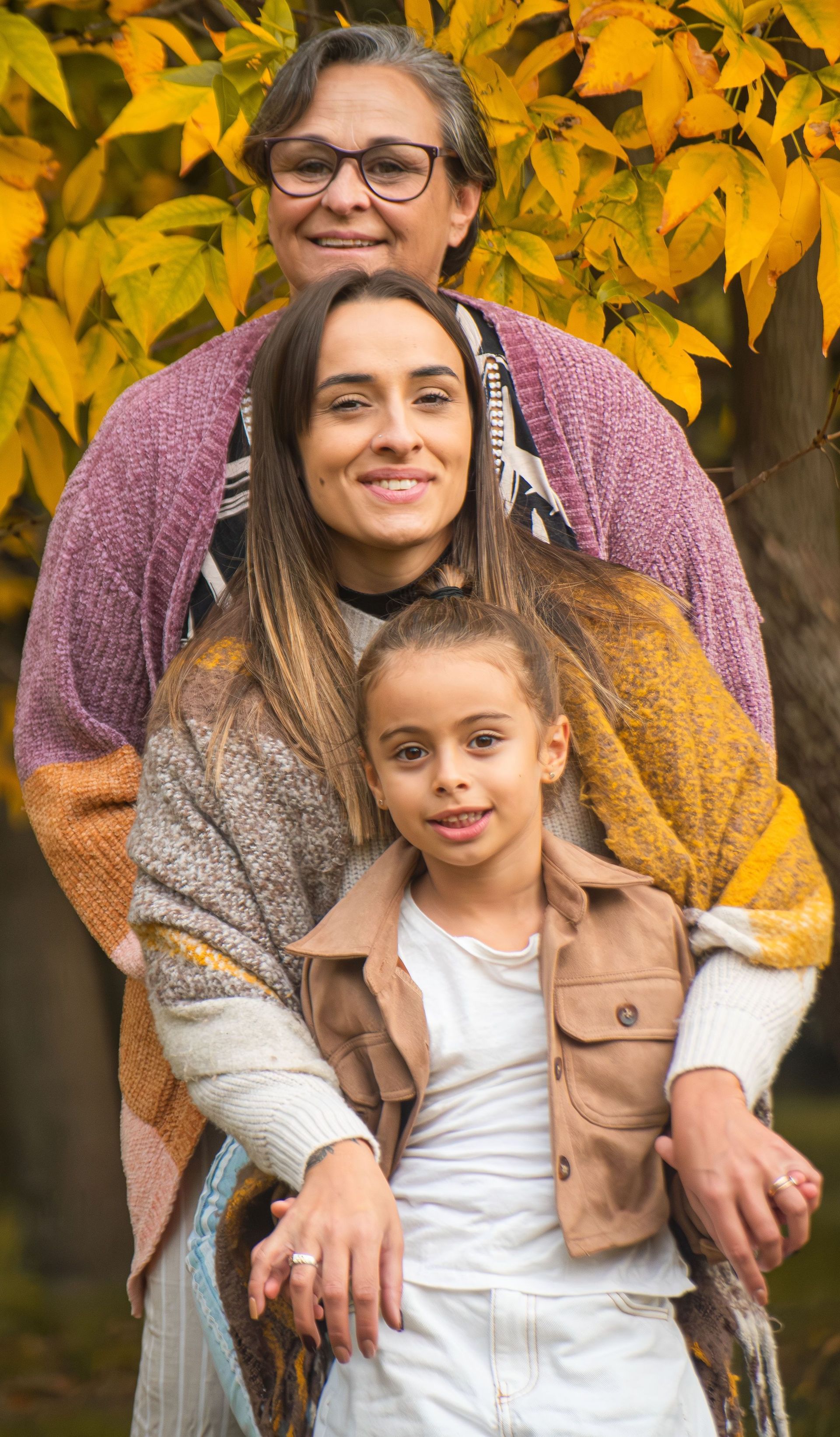 Three people seated outdoors in autumn, with yellow leaves behind them.