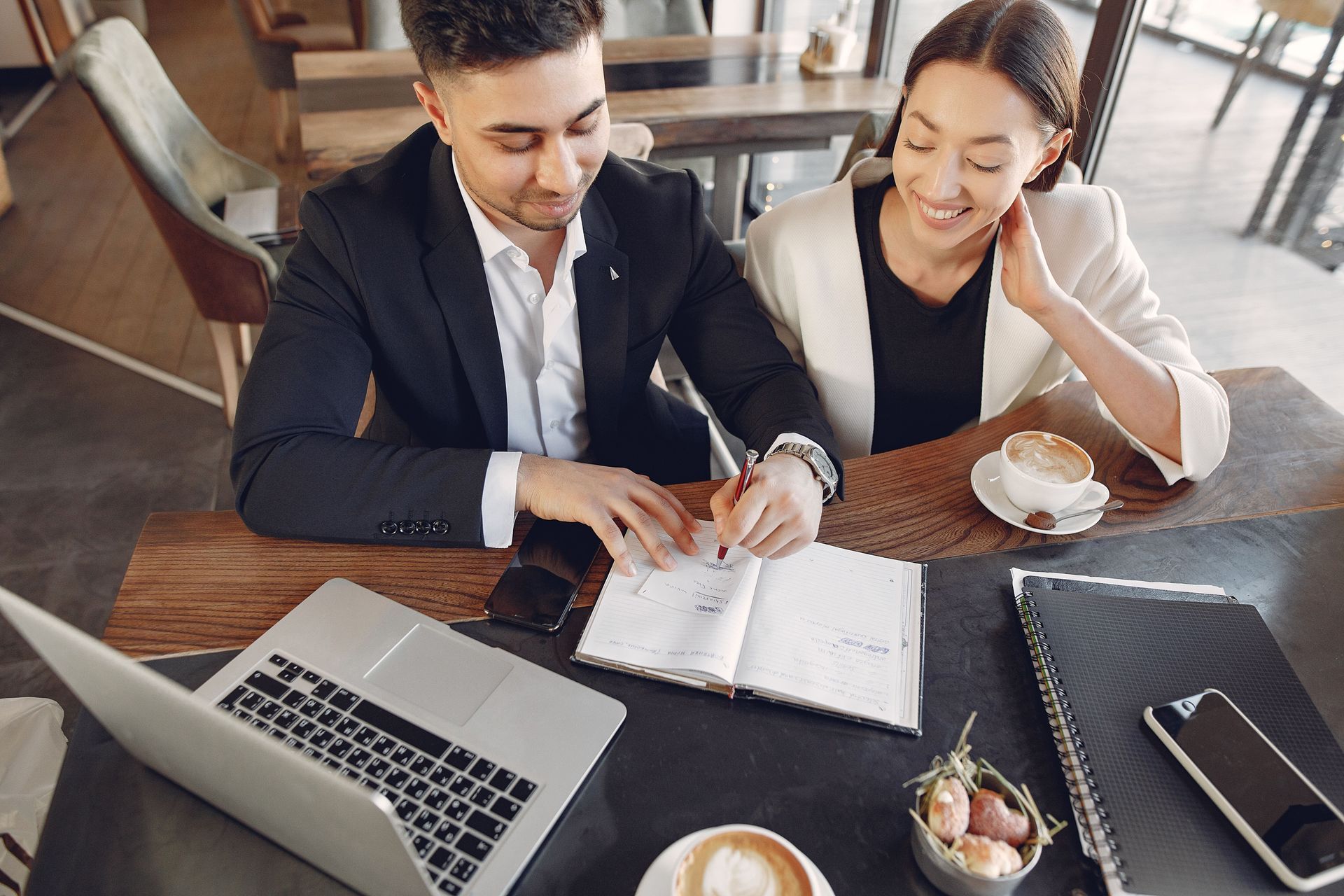 Two coworkers reviewing documents at a desk with a laptop and coffee cups