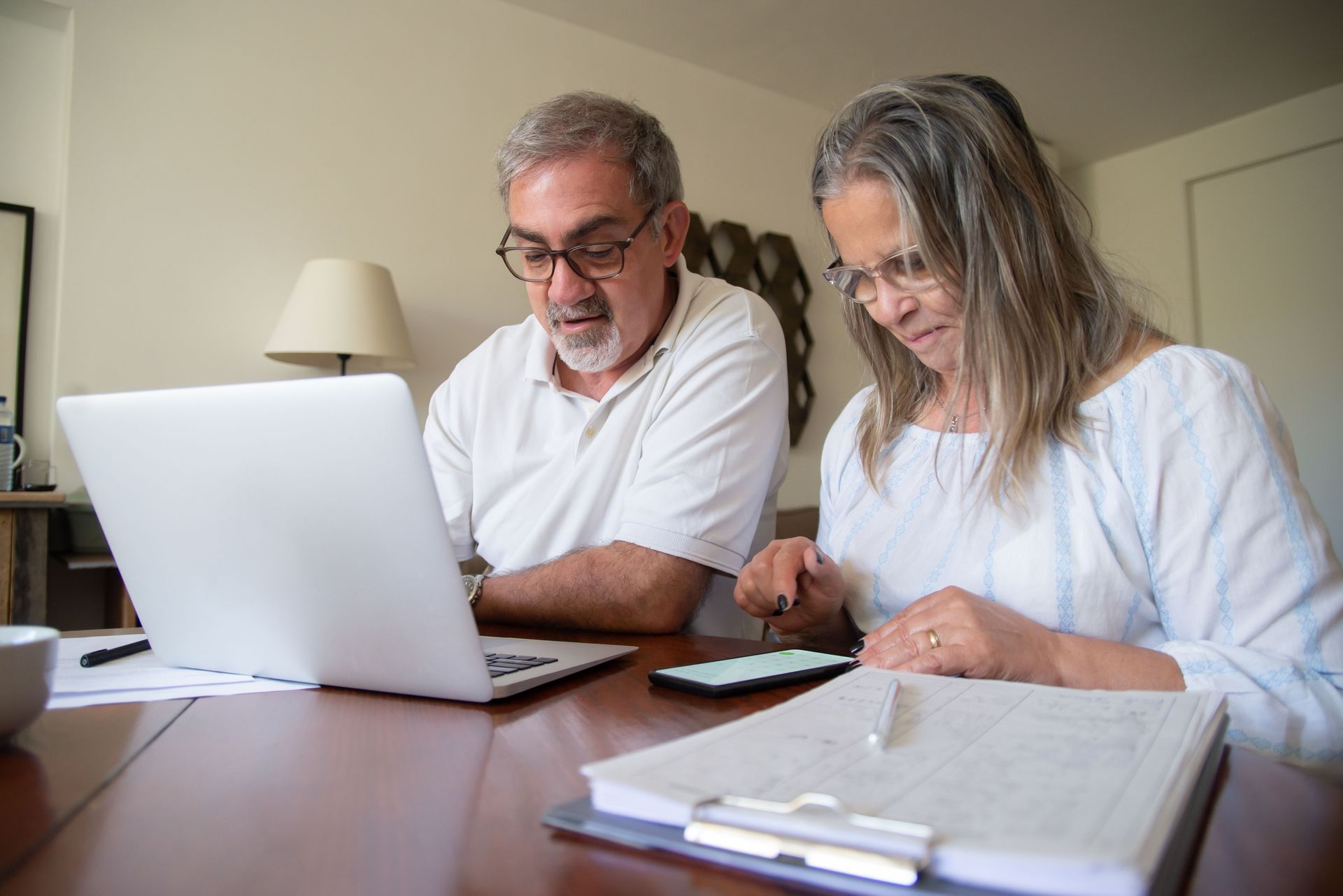 Two adults reviewing paperwork at a table with a laptop in a bright room