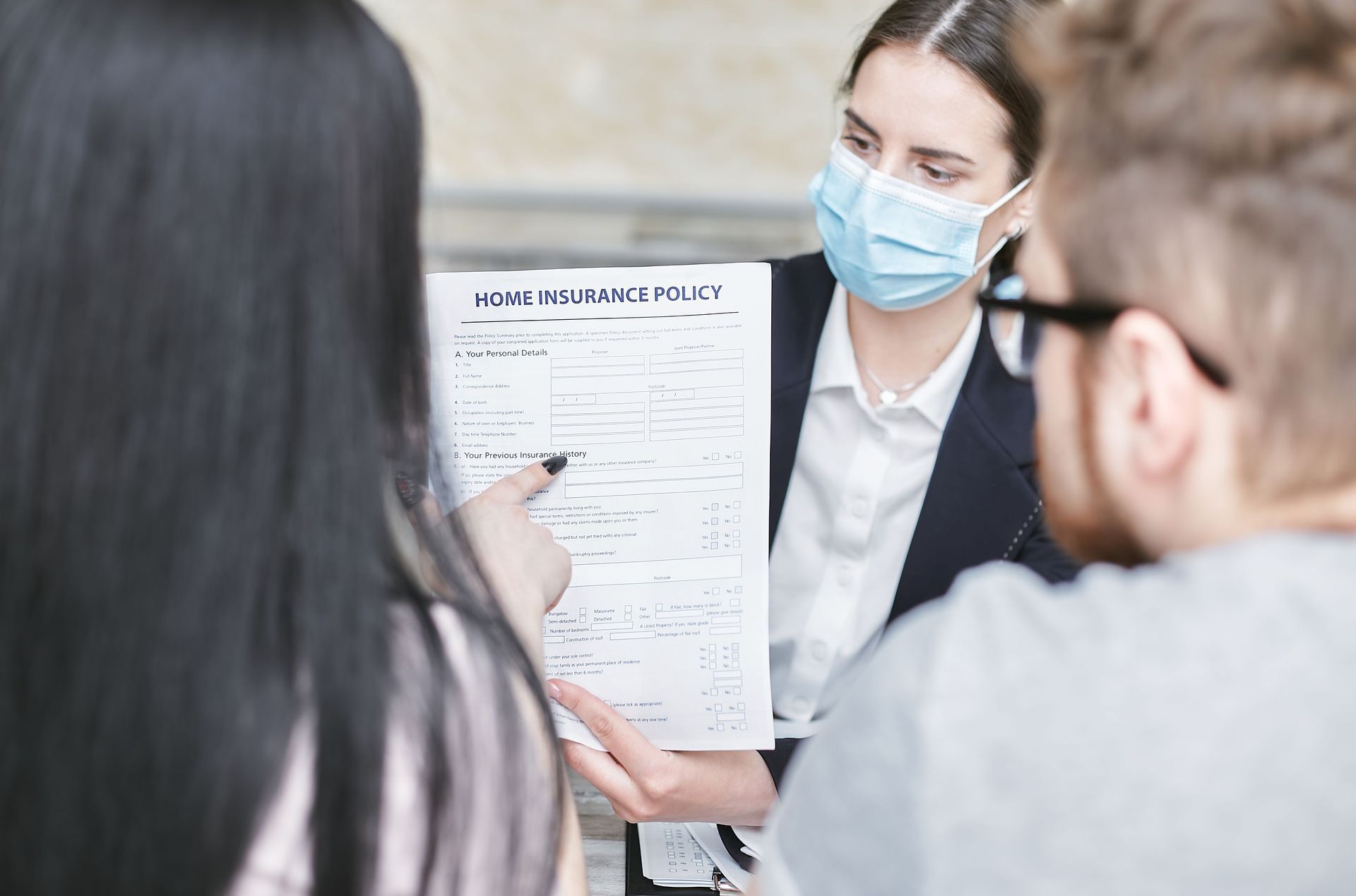 Woman in a blue mask showing a document to two people in a meeting room