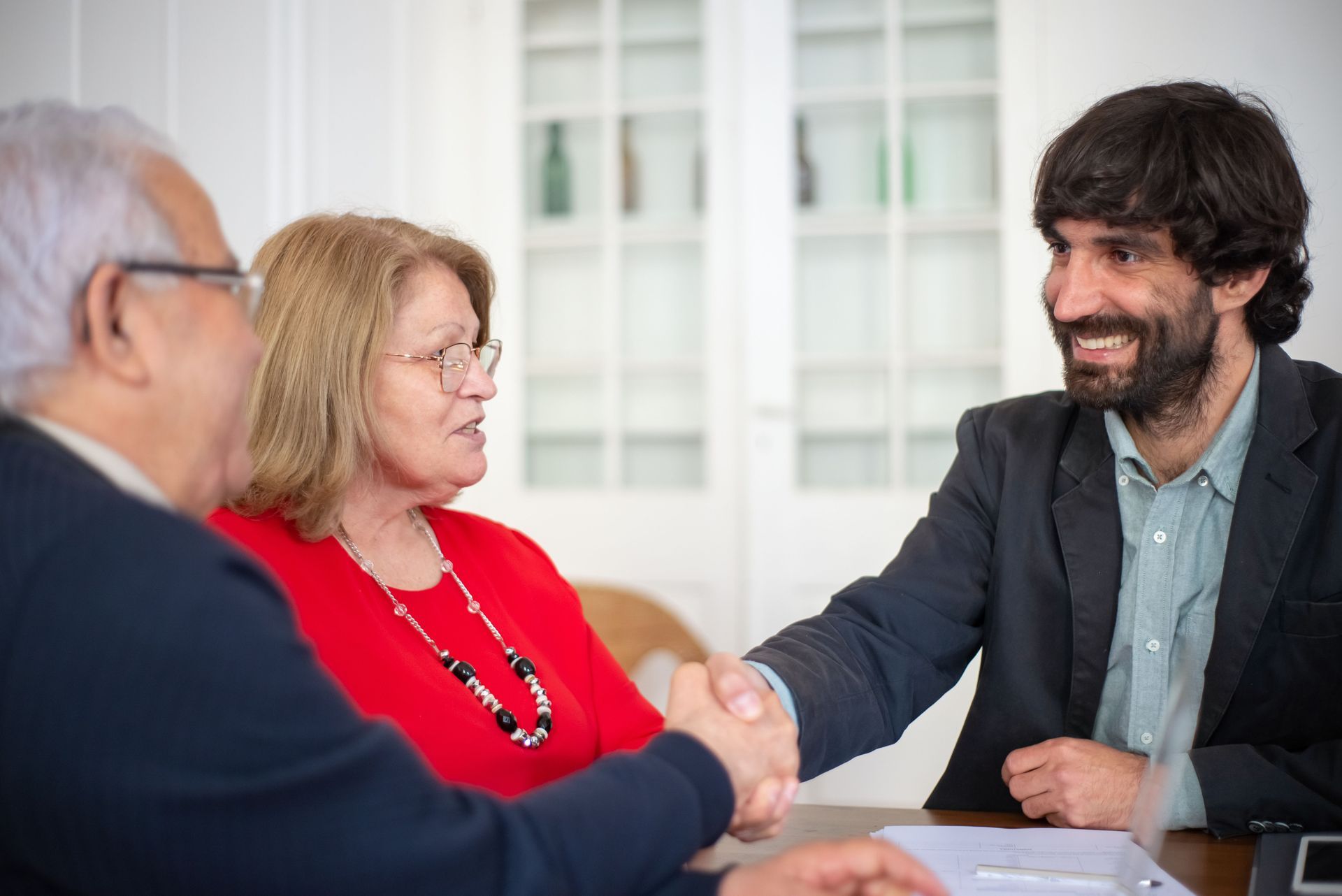 Three people in a meeting shake hands across a table in a bright office