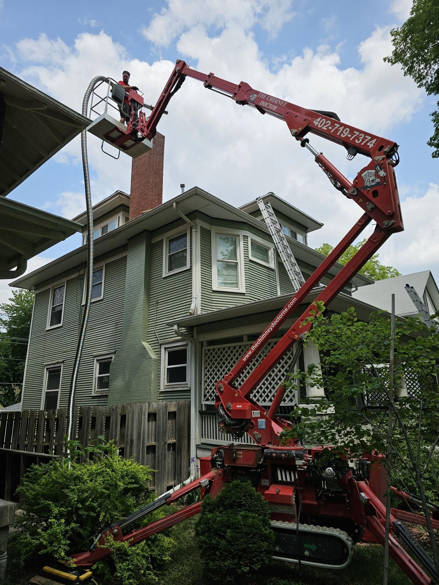 a man is working on a chimney on top of a house with a crane .