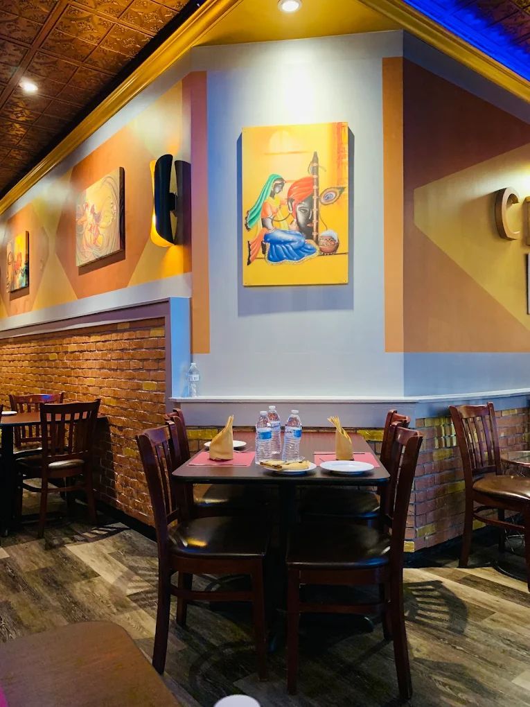 Restaurant interior with round tables set for dining, red tablecloths, black chairs, and dark red walls.