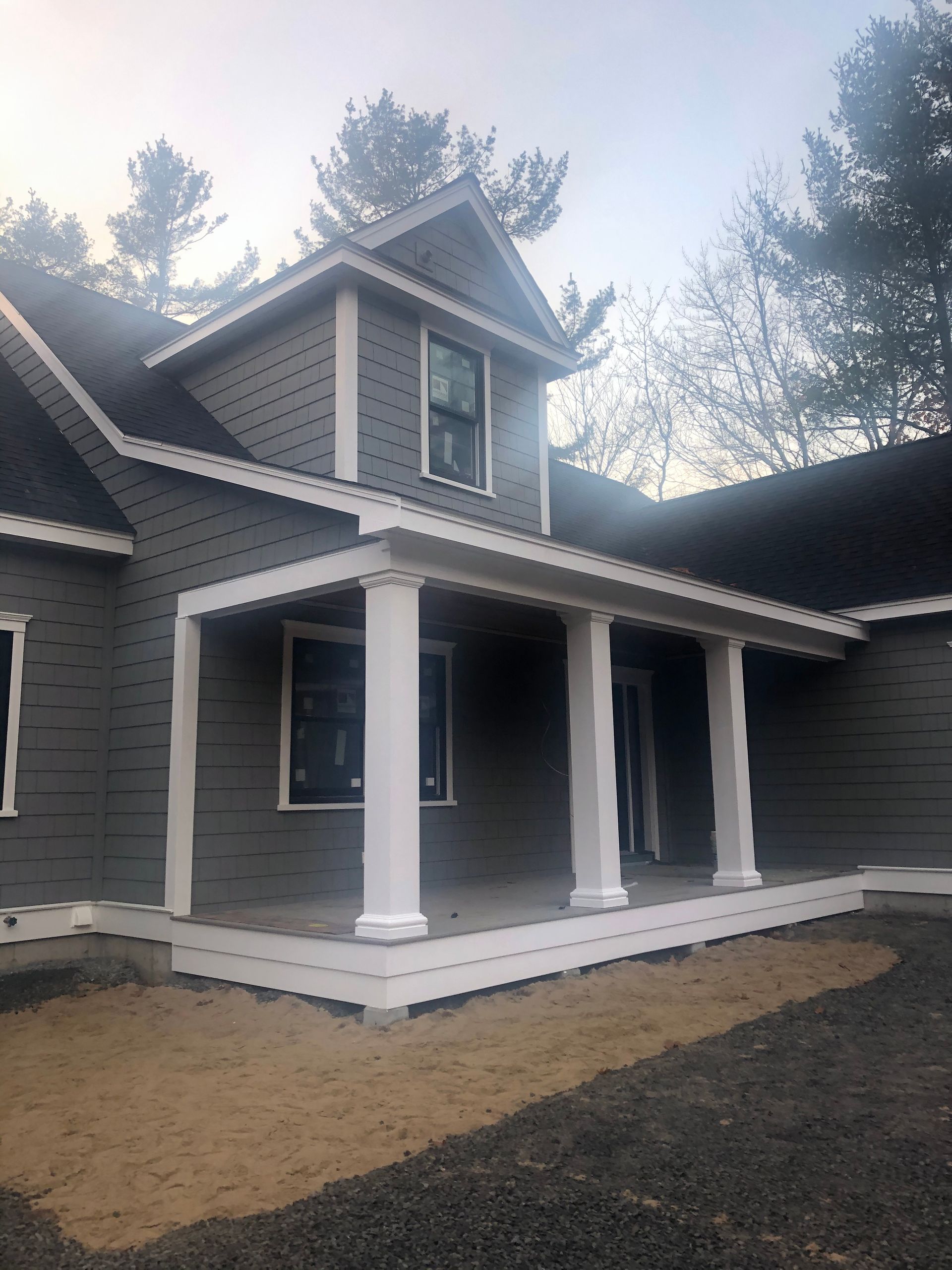 A gray house with a white porch and trees in the background