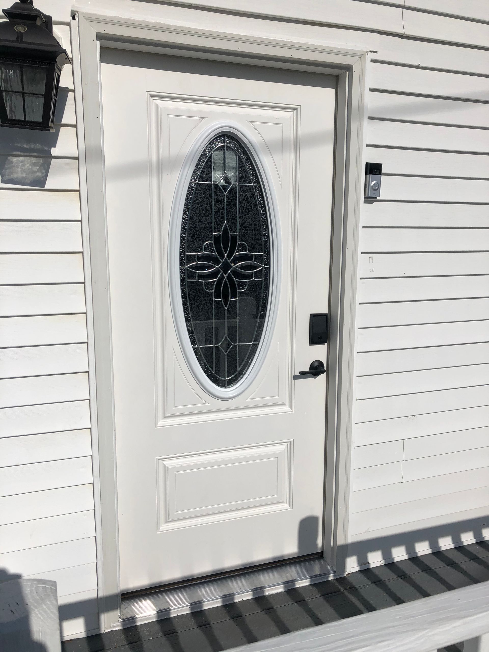 A white door with a stained glass window is on a white house.