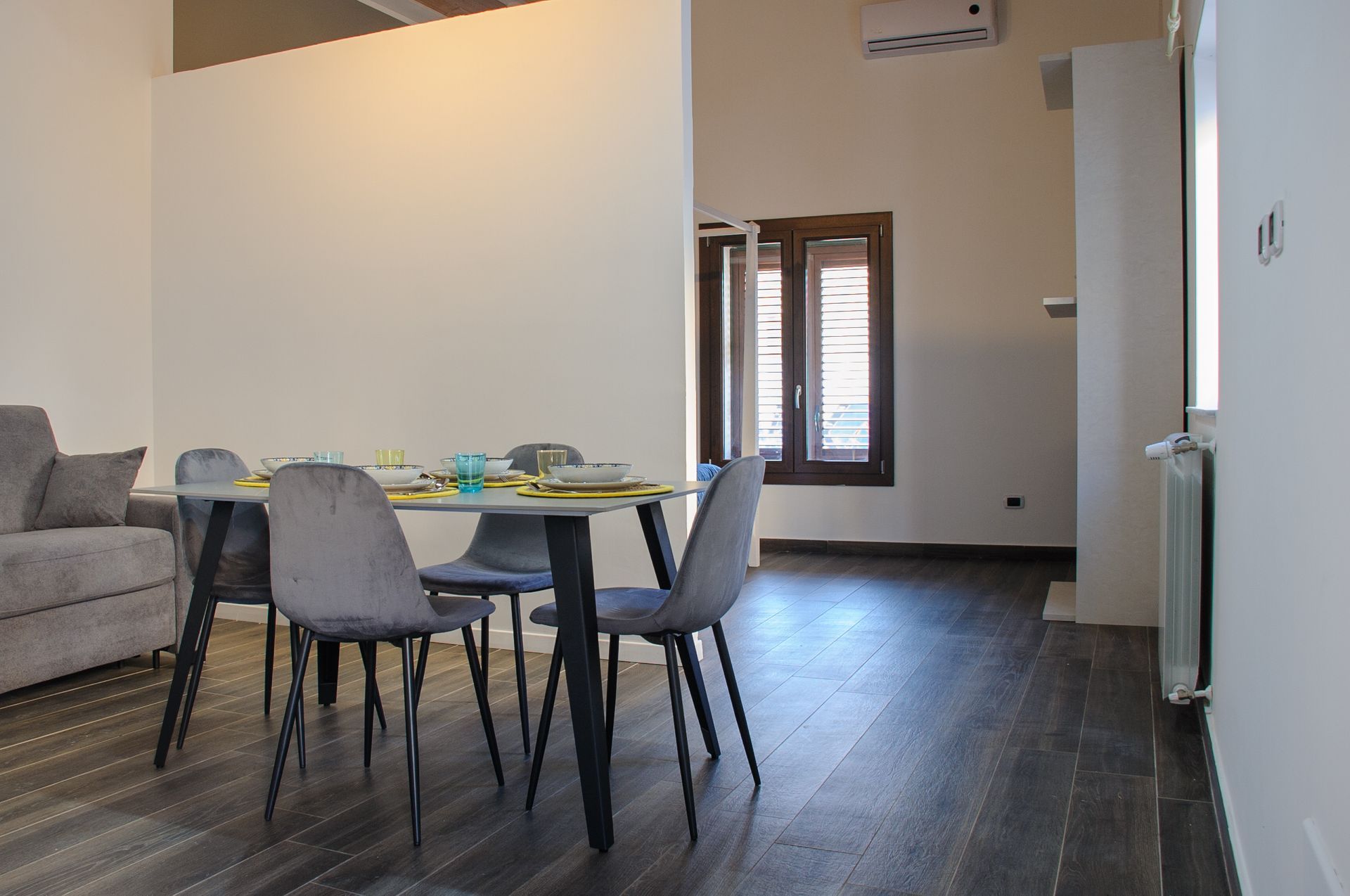 Sala da pranzo moderna con tavolo, sedie grigie, pavimento in legno scuro e ampie finestre.