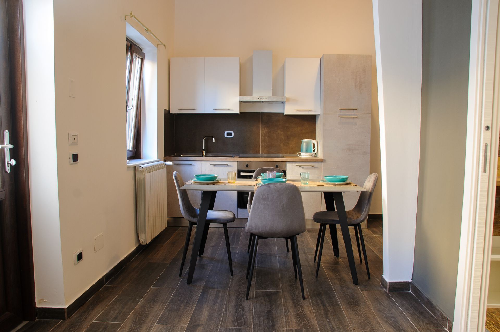 Cucina moderna e zona pranzo con tavolo, sedie, mobili bianchi e pavimento in legno scuro.