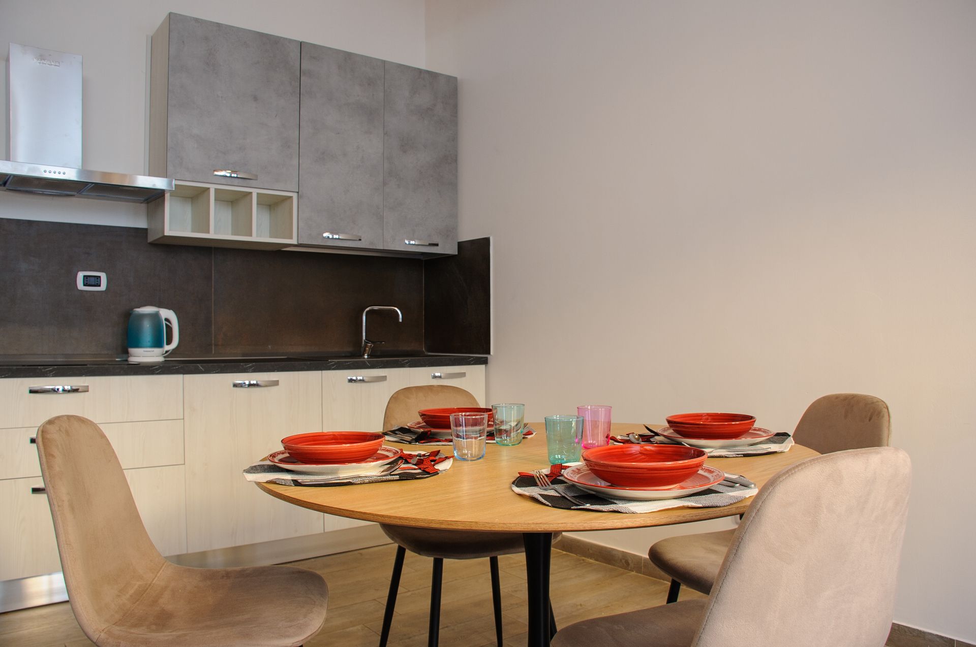 Cucina moderna con tavolo da pranzo, piatti rossi e sedie beige.