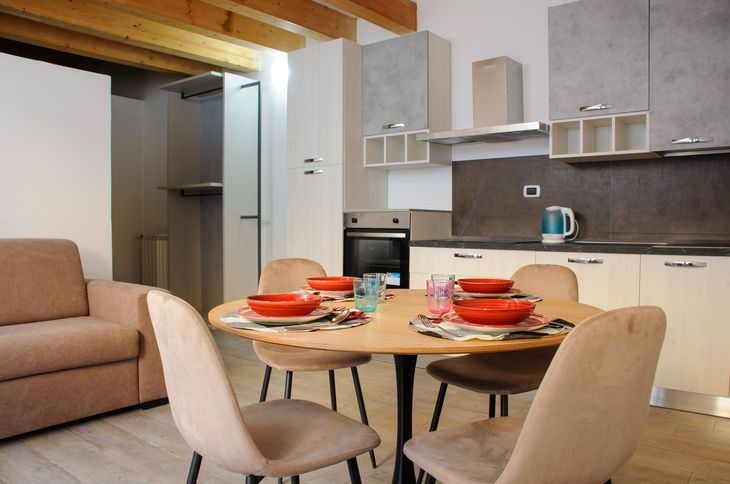 Moderna zona pranzo a pianta aperta con tavolo per quattro persone accanto a una cucina compatta e divano.