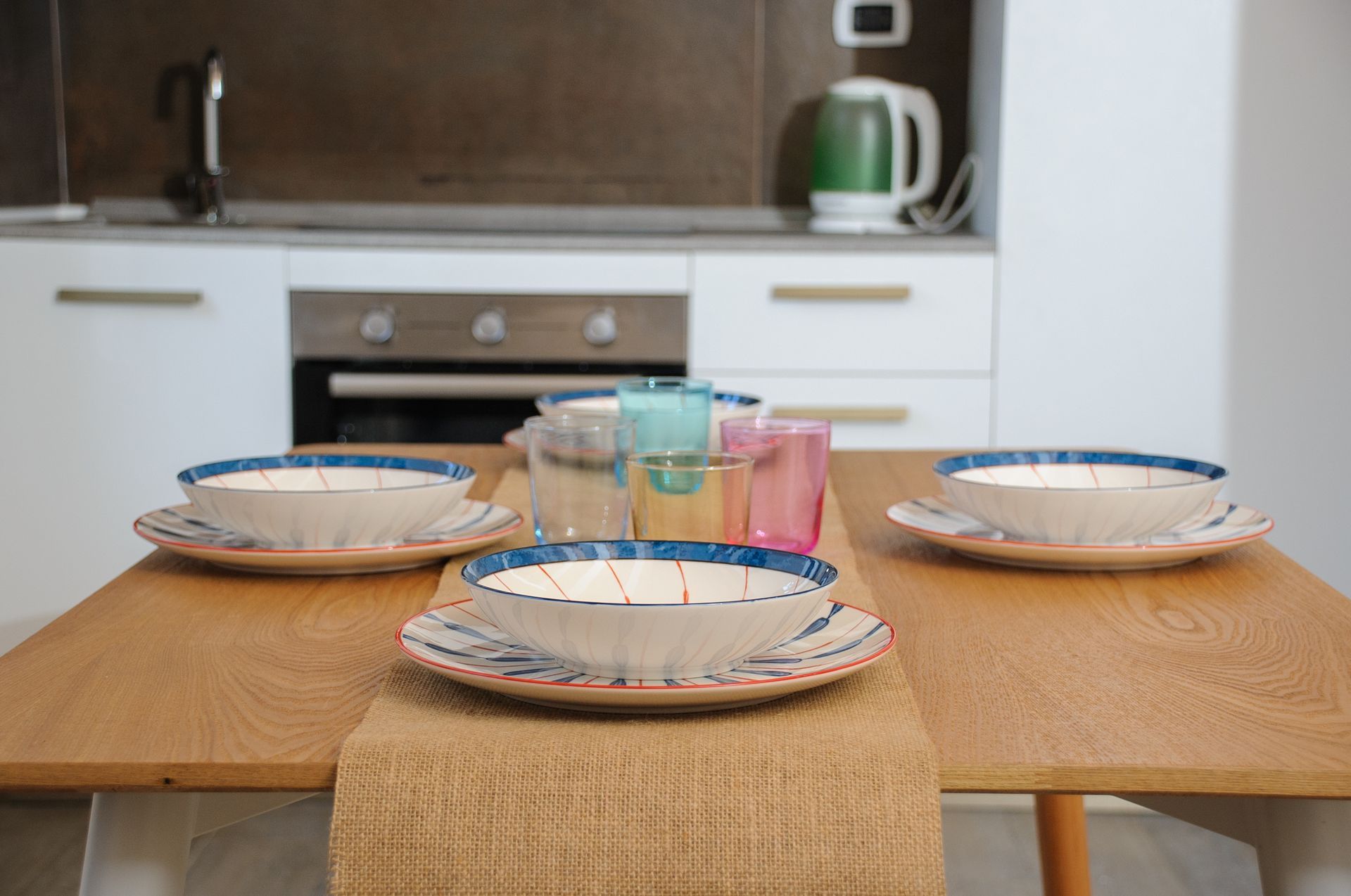 Tavola apparecchiata in una cucina moderna con piatti e bicchieri colorati su un tavolo di legno.