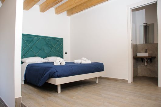 Camera da letto minimalista con testiera color verde acqua, copriletto blu e porta del bagno