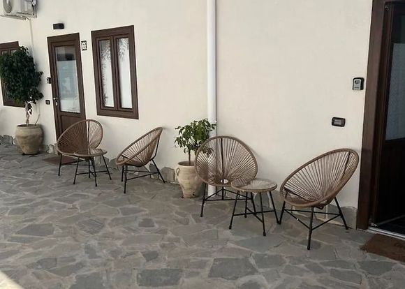 Patio esterno con sedie in vimini e tavolini lungo una parete color crema dell'edificio.